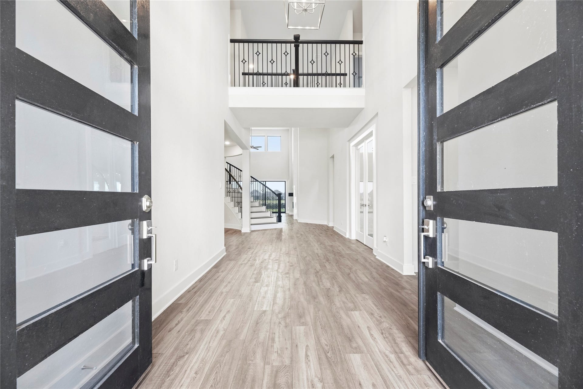 10314 Forest Lake Drive, Missouri City, TX 77459 Grand entrance showcasing glass-panel double doors, soaring two-story ceilings, open iron-railed overlook, and a clear line of sight to the back living space.