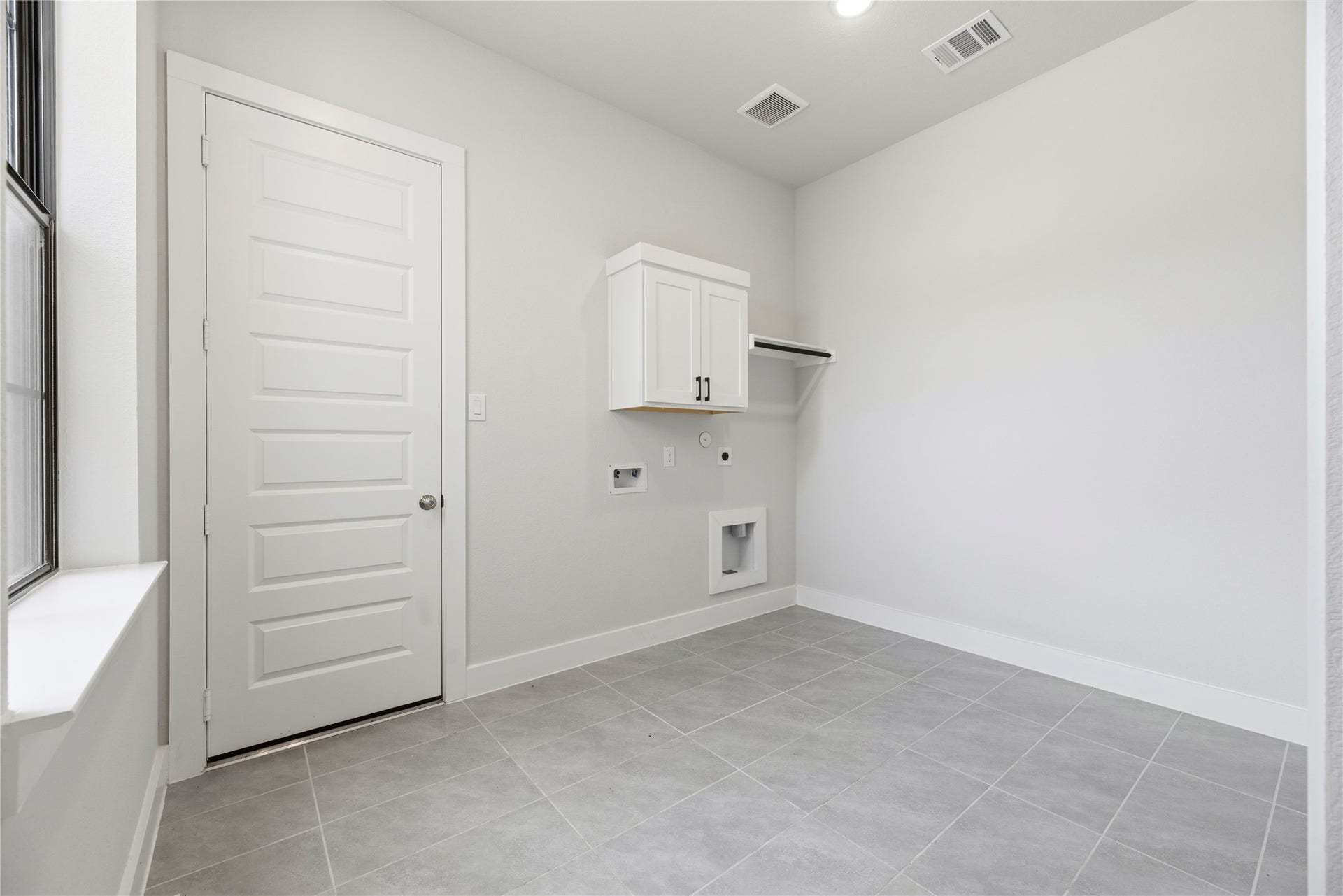 10314 Forest Lake Drive, Missouri City, TX 77459 Dedicated utility room featuring easy-maintenance tile flooring, upper storage cabinetry with hanging rod, washer/dryer hookups, and natural window lighting.