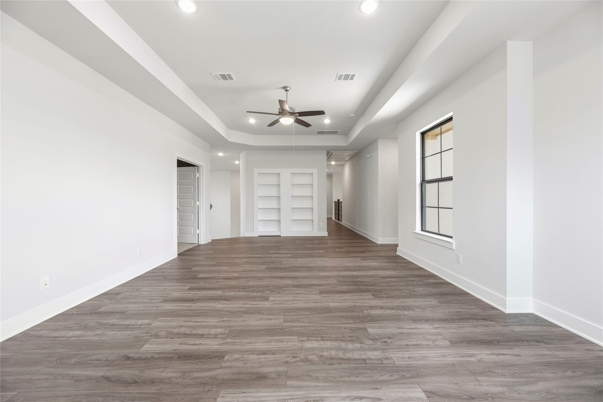10314 Forest Lake Drive, Missouri City, TX 77459 Generous game room featuring tray ceilings, wood-look flooring, and custom built-in white shelving along the rear wall.