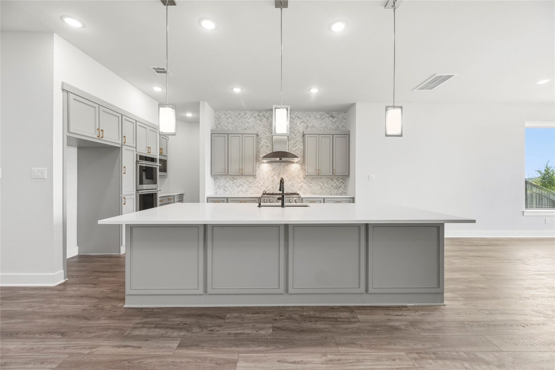 10314 Forest Lake Drive, Missouri City, TX 77459 Center view of the massive prep island with built-in sink, dark hardware accents, triple glass pendant lights, and stainless steel range hood setup.