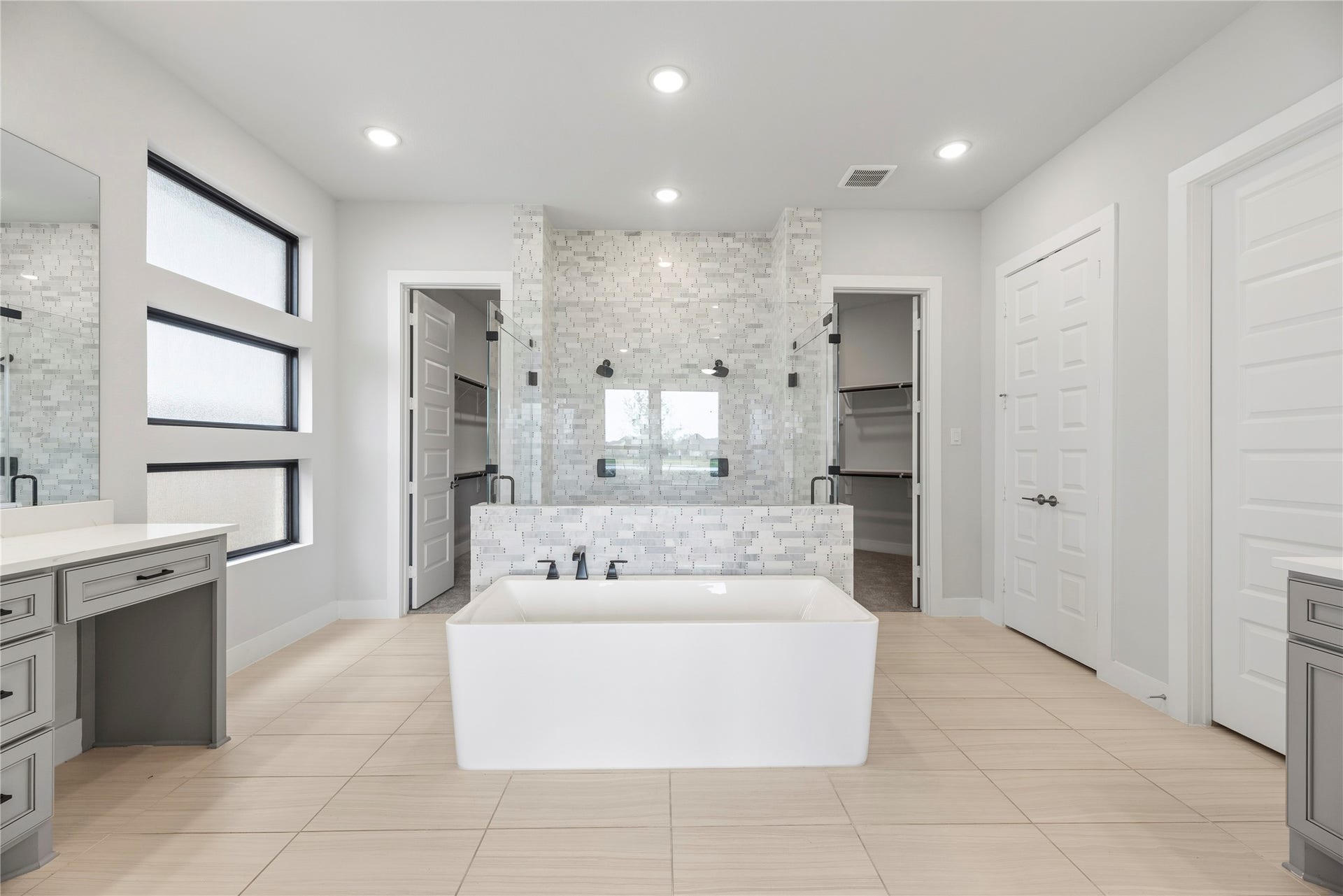 10314 Forest Lake Drive, Missouri City, TX 77459 Luxurious primary bath showcase featuring a modern freestanding soaking tub, mosaic tile feature wall, walk-in shower with dual heads, split dual vanities, and dual walk-in closets.