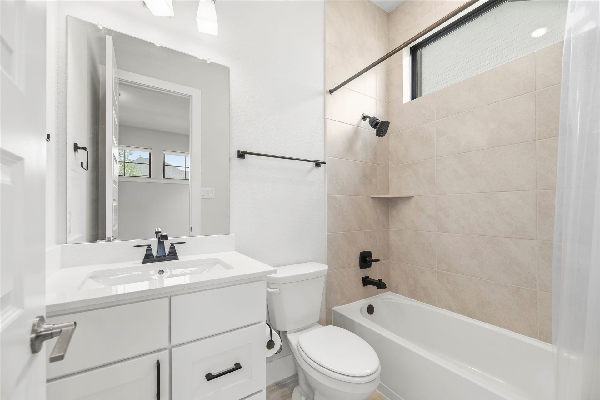 10314 Forest Lake Drive, Missouri City, TX 77459 Clean, modern full bath featuring a white vanity with quartz counter, dark matte fixtures, and a tiled tub/shower combo with a natural light transom window.