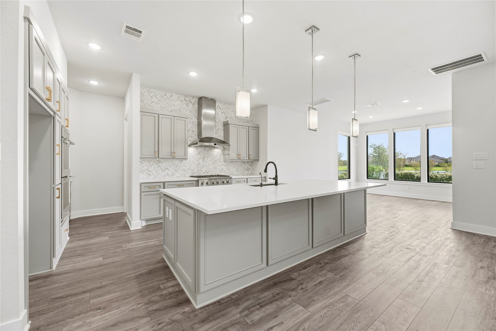10314 Forest Lake Drive, Missouri City, TX 77459 Modern chef's kitchen featuring soft-grey shaker cabinetry, quartz countertops, a large seating island, modern pendant lighting, and herringbone tile backsplash.