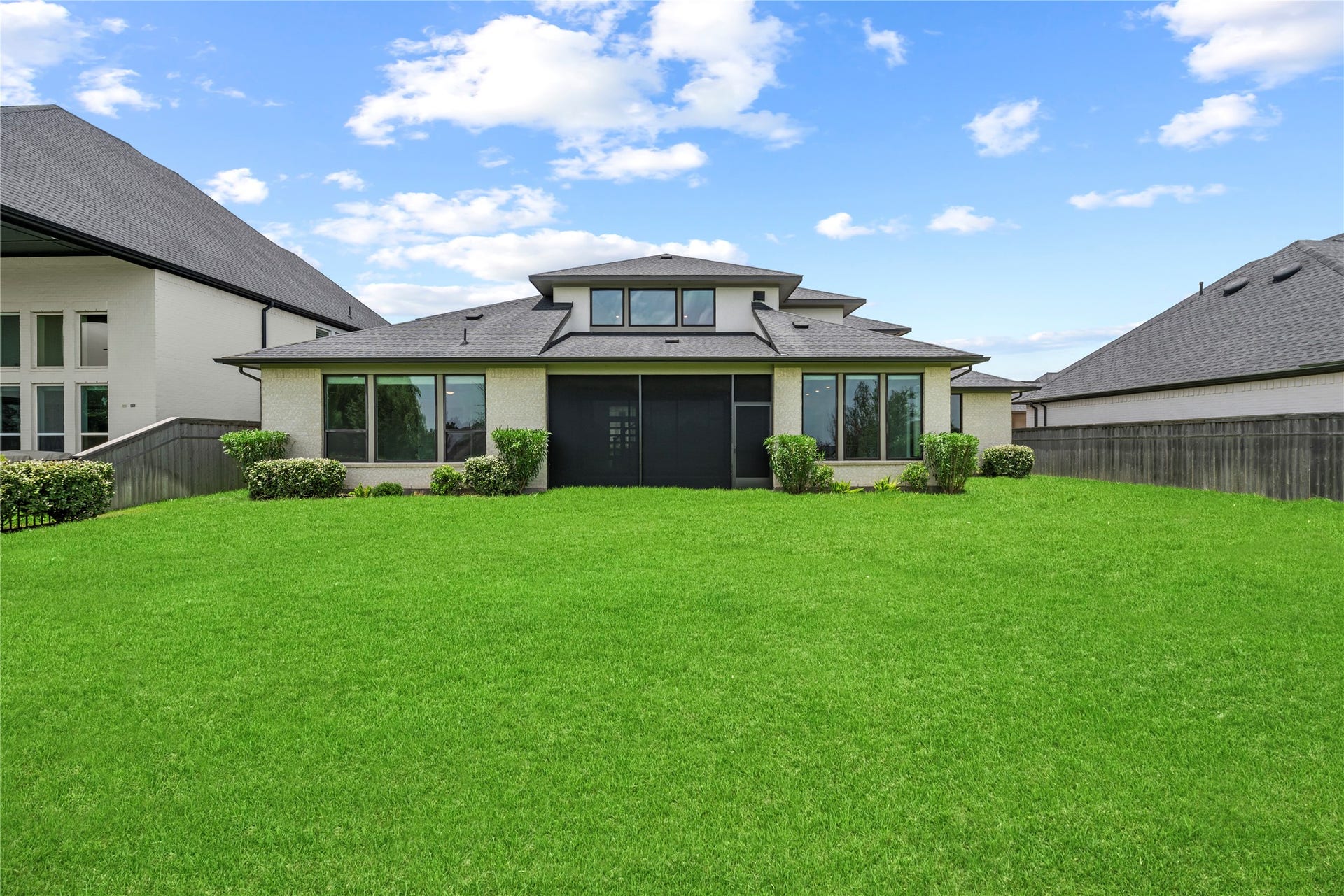 10314 Forest Lake Drive, Missouri City, TX 77459 Direct back view showcasing the home's contemporary rooflines, brick and stucco finishes, screened patio, and flat, lush lawn.