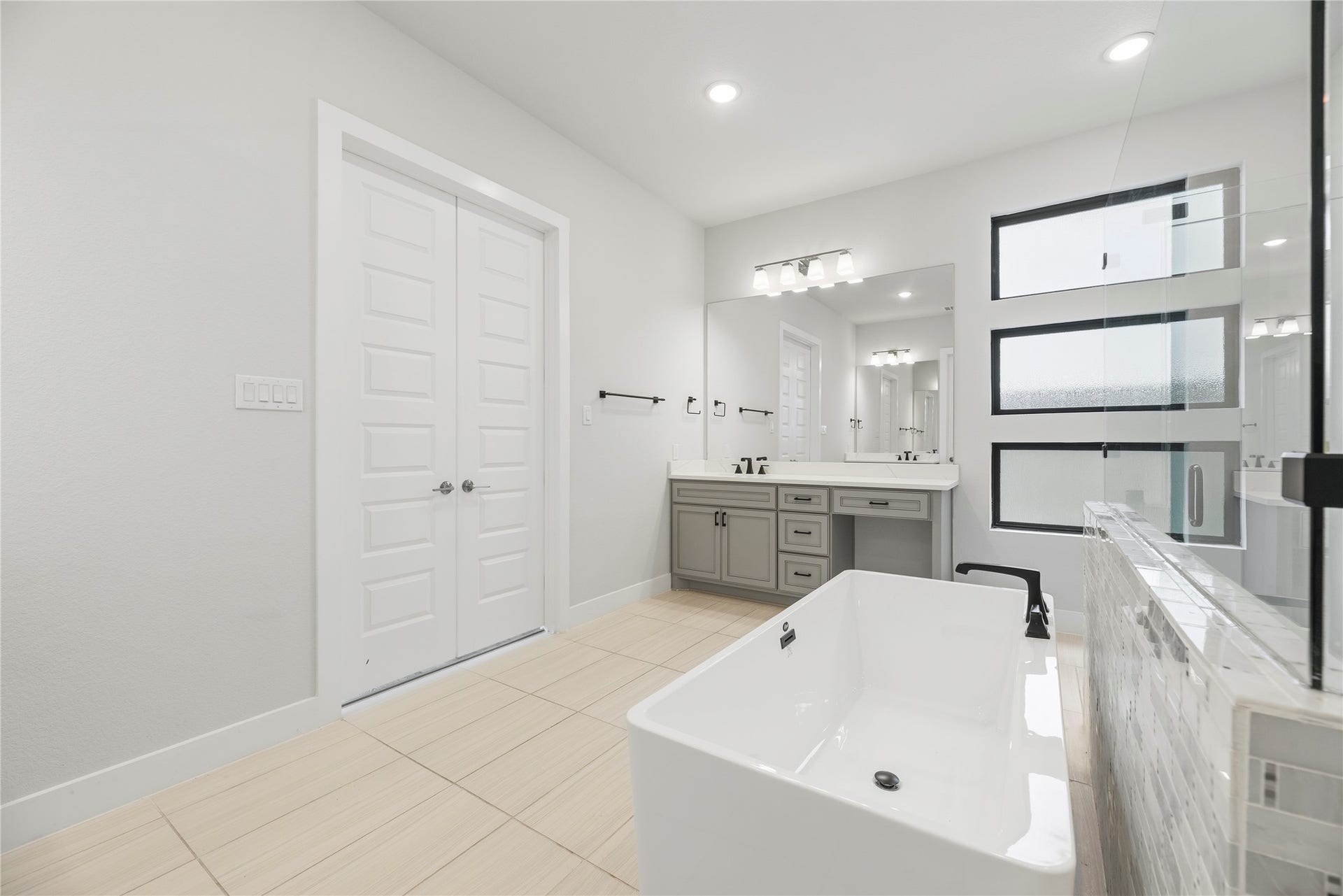 10314 Forest Lake Drive, Missouri City, TX 77459 Angle highlighting the standalone tub, matte black plumbing hardware, neutral floor tile, and three stacked frosted privacy windows above the vanity.