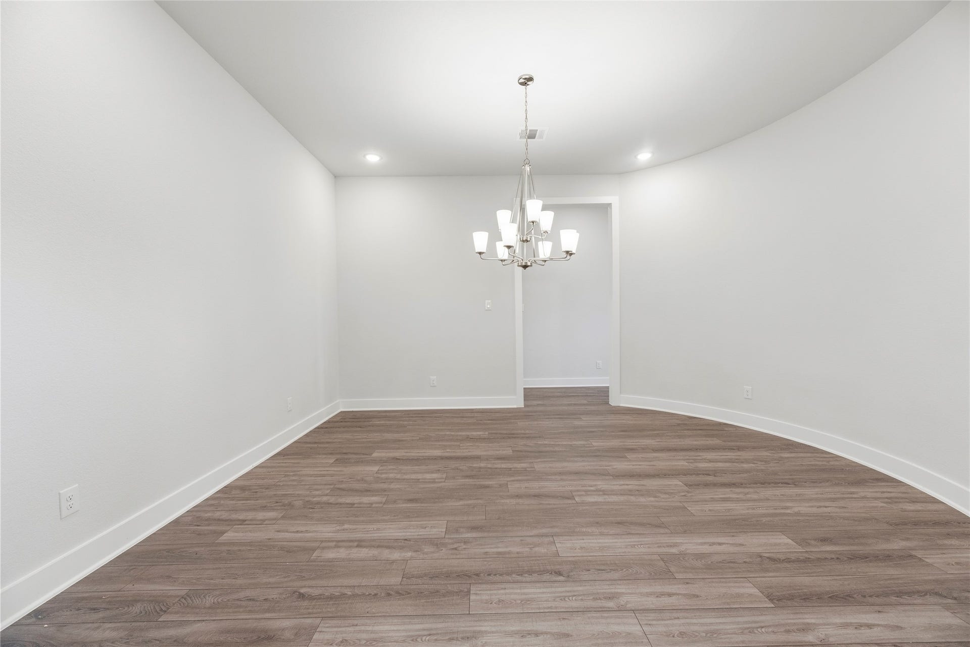 10314 Forest Lake Drive, Missouri City, TX 77459 Elegant dining area showcasing a multi-light chandelier, smooth wood-look plank flooring, and a subtle curved architectural accent wall.