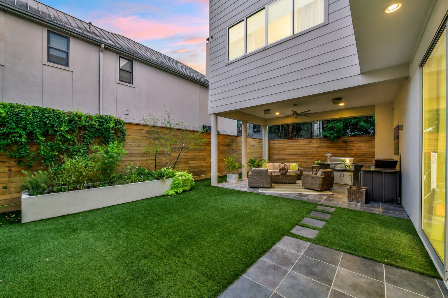 2302 Persa Street, Houston, TX 77019 The private sanctuary features vibrant synthetic turf bordered by modern, sophisticated planters for sleek, high-end landscaping. Complete with a covered patio area, recessed ceiling lights, and outdoor kitchen.
