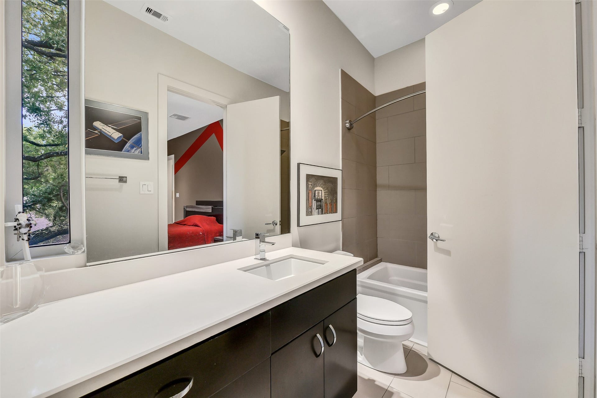 2302 Persa Street, Houston, TX 77019 This sleek ensuite bathroom features a long white countertop vanity with dark cabinetry, modern chrome fixtures with direct access to a dedicated walk-in closet.