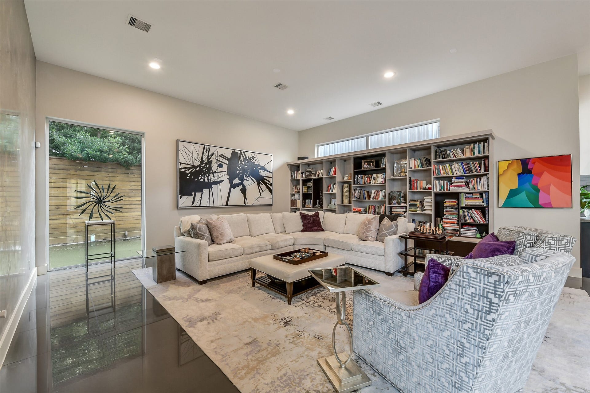 2302 Persa Street, Houston, TX 77019 The spacious, light-filled family room features a stunning full-length built-in bookshelf that serves as both a dramatic focal point and functional display. Expansive windows and glass doors fill the space with natural light while offering views of the private outdoor courtyard, creating an inviting atmosphere ideal for relaxation and entertaining.