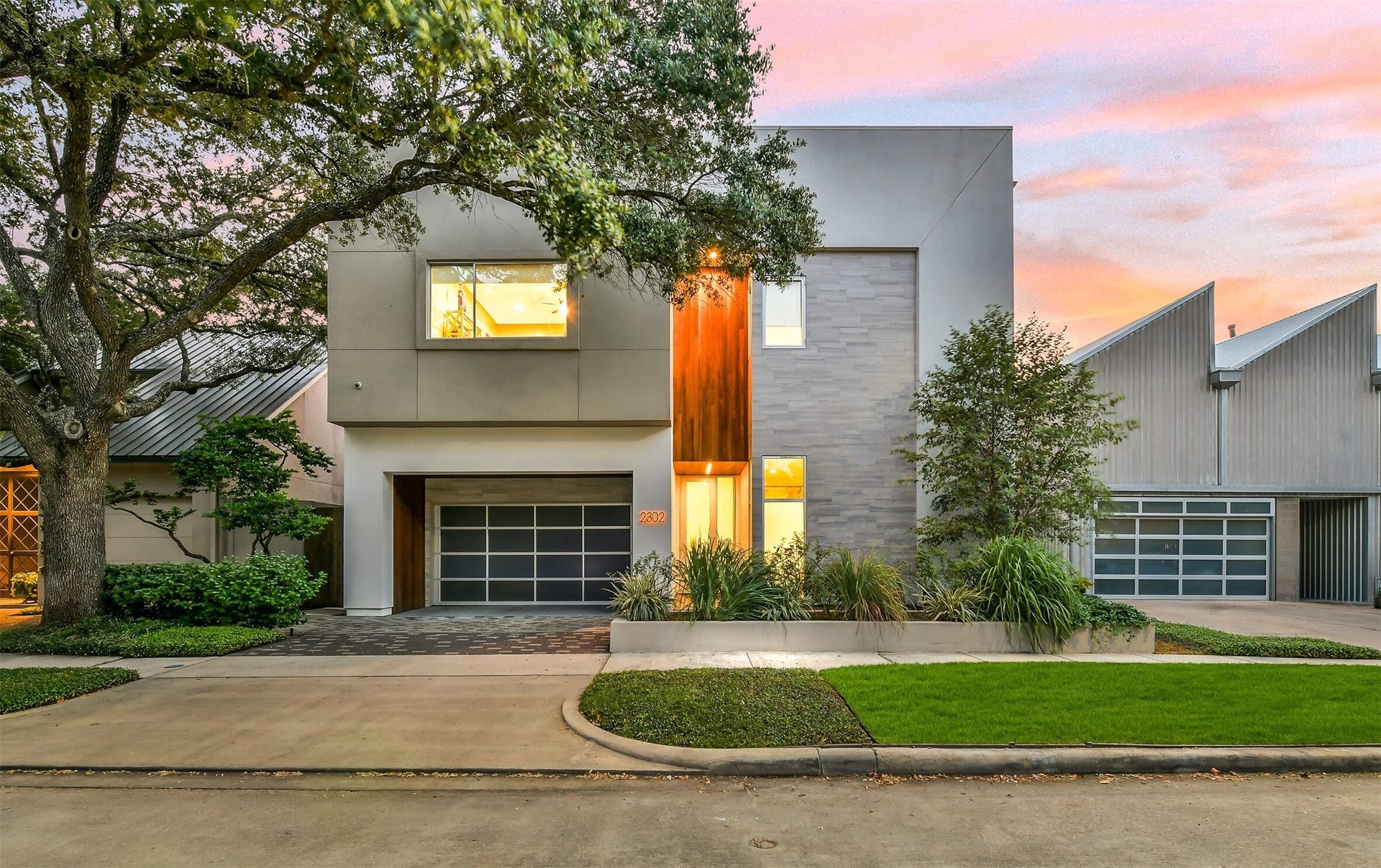 2302 Persa Street, Houston, TX 77019 A sleek glass-panel garage door, paved drive, and integrated raised planters complement the homes striking multi-textured exterior, creating an inviting, sophisticated approach to the residence.