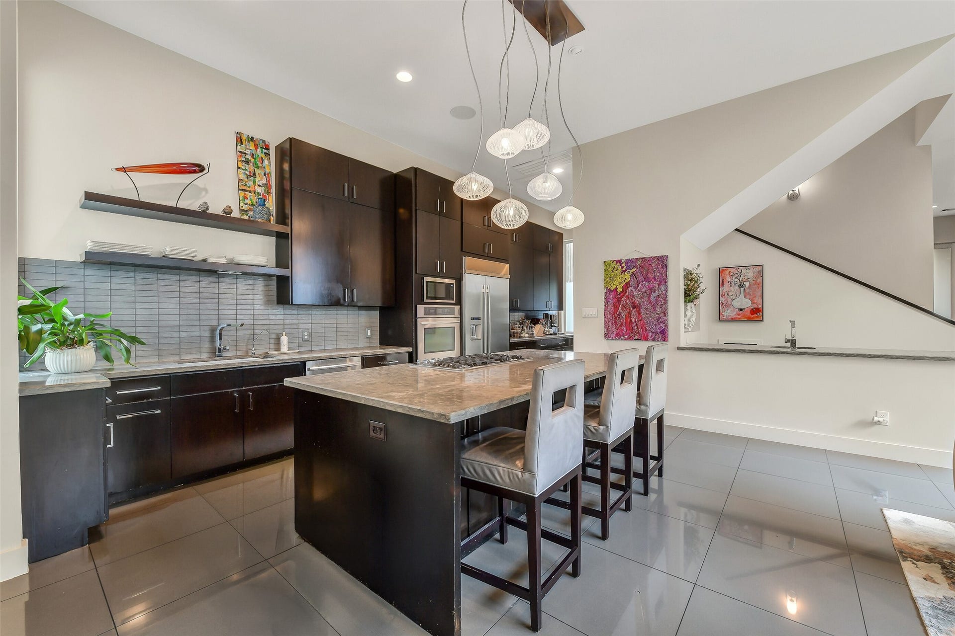 2302 Persa Street, Houston, TX 77019 This is another view of the chef-inspired kitchen featuring a large island, sleek dark cabinetry, polished floors, and custom pendant lighting. Home features a wet bar that is perfect for entertaining.
