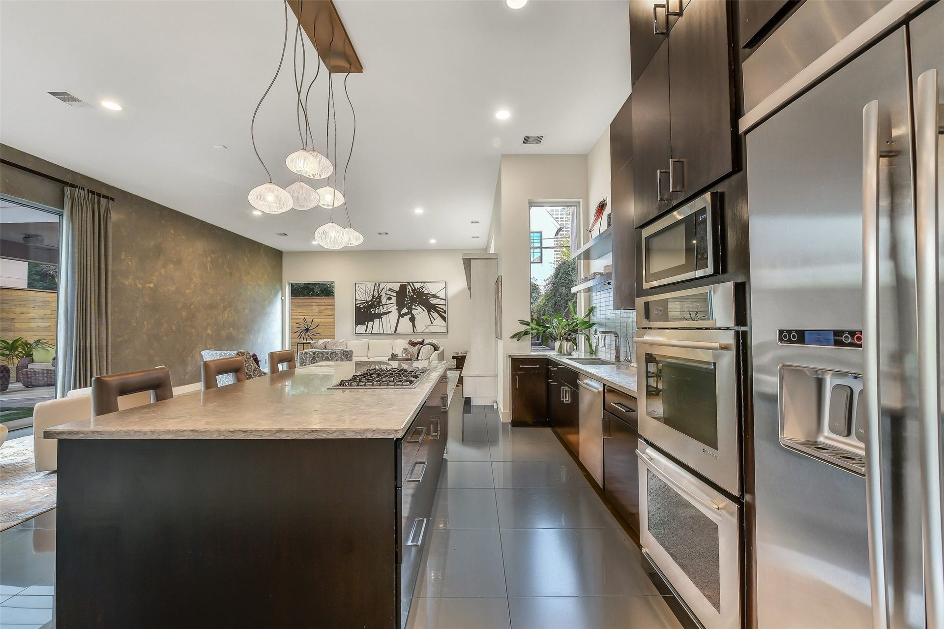 2302 Persa Street, Houston, TX 77019 Anchored by an expansive center island with sleek dark cabinetry and polished stone countertops, this gourmet kitchen blends high-end stainless steel appliances with clean architectural lines for a sophisticated design.