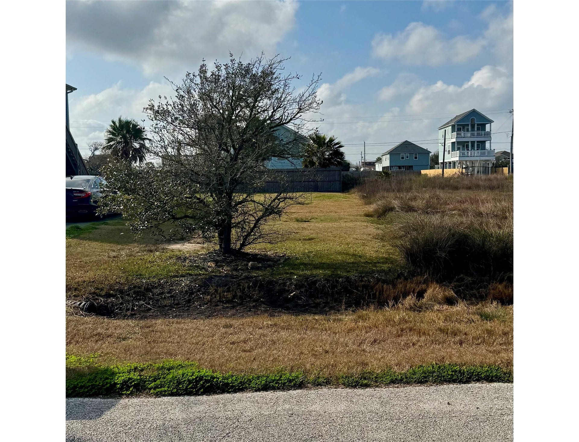 1022 19th Street, San Leon, TX 77539 This photo shows a grassy vacant lot with a lone tree in the center, surrounded by a few houses and a fence. The lot is across the street from the waterfront.