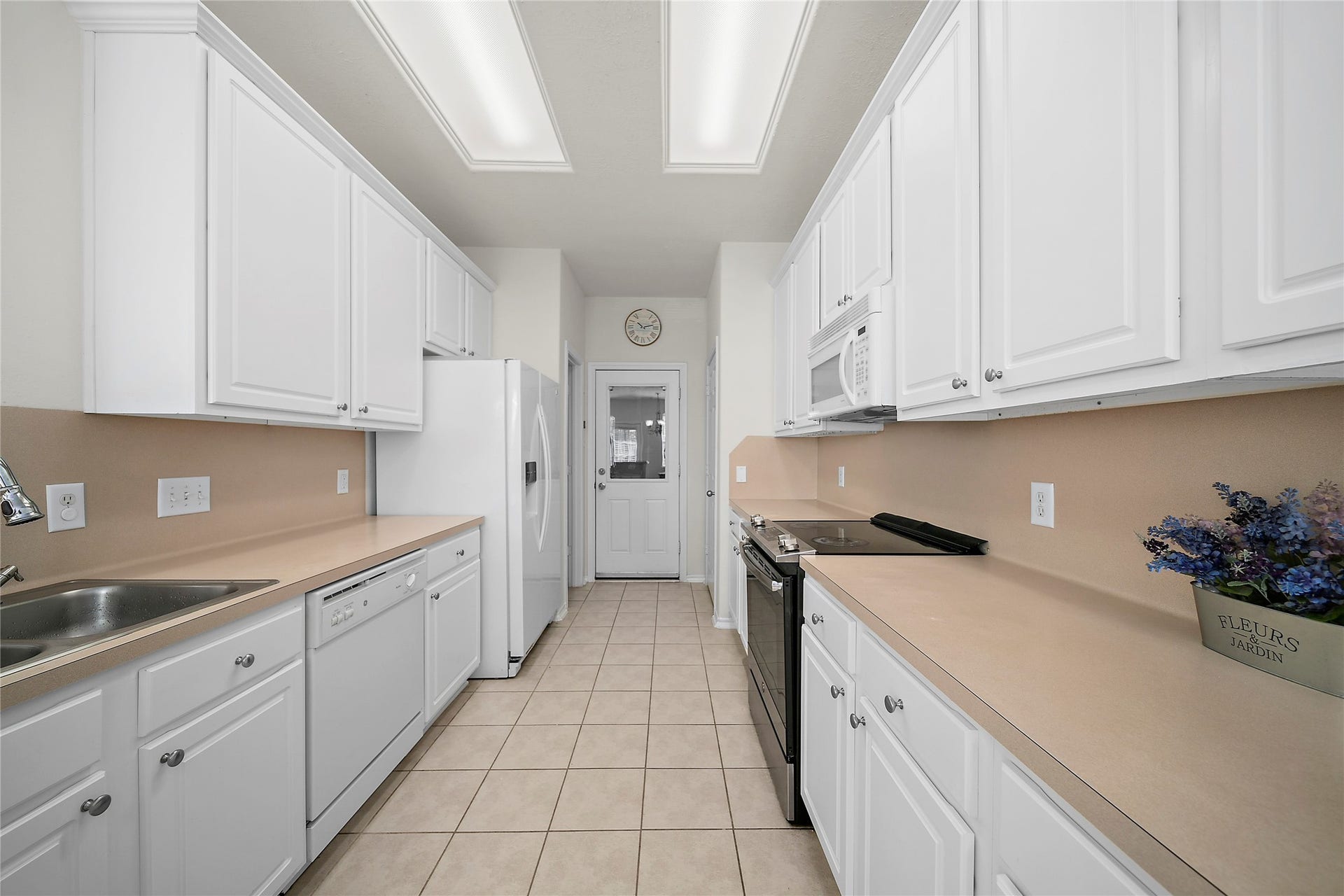 Bright, open living space with wood flooring and large windows. Features a dining area with a bench-style table, a cozy daybed, and a piano. The kitchen has white cabinetry and a breakfast bar, adding functionality and charm.