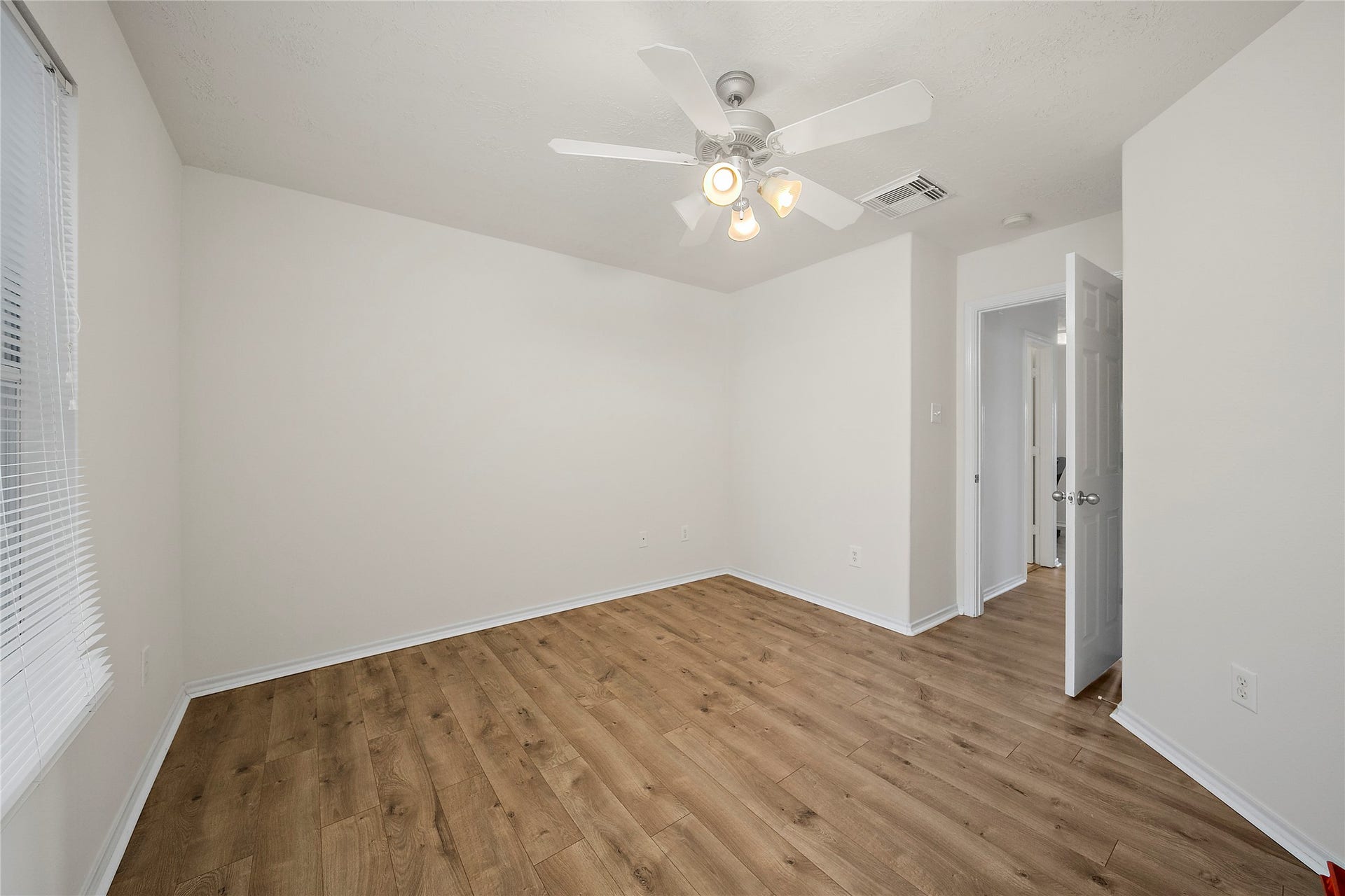 This photo shows a bright, open-concept living area with a blend of hardwood and tile flooring. The kitchen features ample white cabinetry and modern appliances, while the adjacent space is perfect for dining or lounging. A ceiling fan and built-in shelving add functionality and comfort.