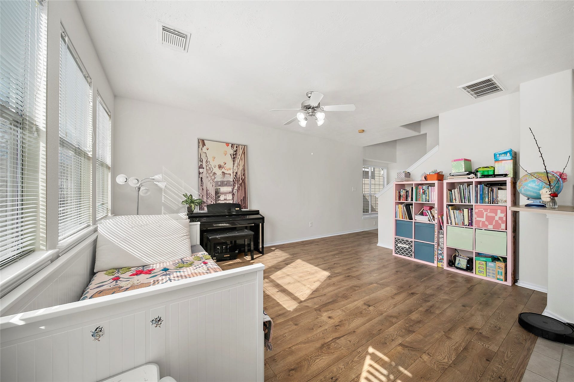 This two-story townhouse features a light beige exterior with white trim and a two-car garage. It is complemented by mature trees and a small front yard, offering a welcoming and shaded entrance.