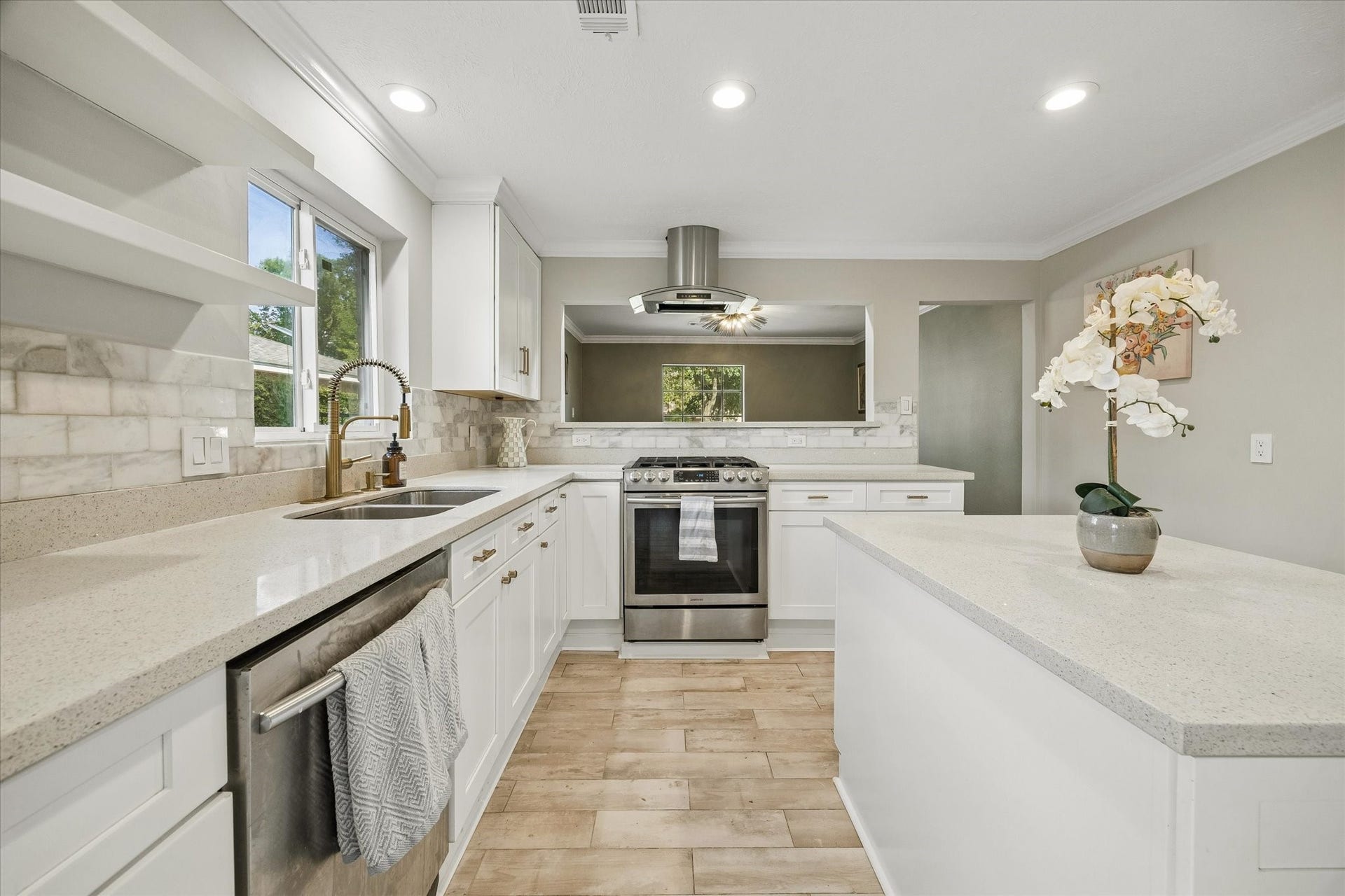 7827 Zilonis Court, Jersey Village, TX 77040 Sleek kitchen island with ample storage, open shelving, and integrated dishwasher, complemented by stainless steel appliances and a stylish gold faucet.