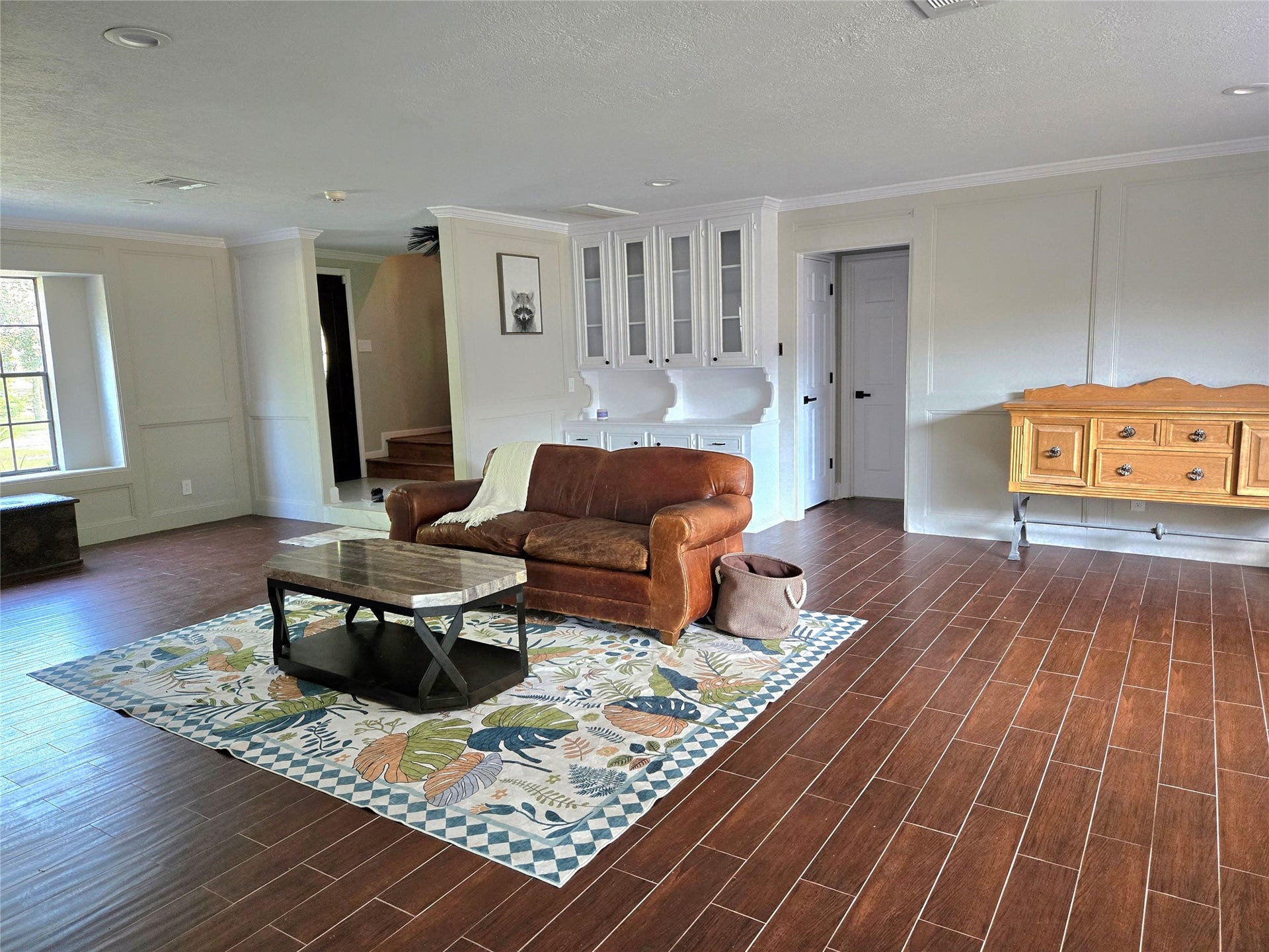 7827 Zilonis Court, Jersey Village, TX 77040 Bright, open-concept living area featuring rich wood-look tile flooring, elegant custom built-ins, abundant natural light, and stylish finishes that create a warm, inviting space perfect for everyday living and entertaining.