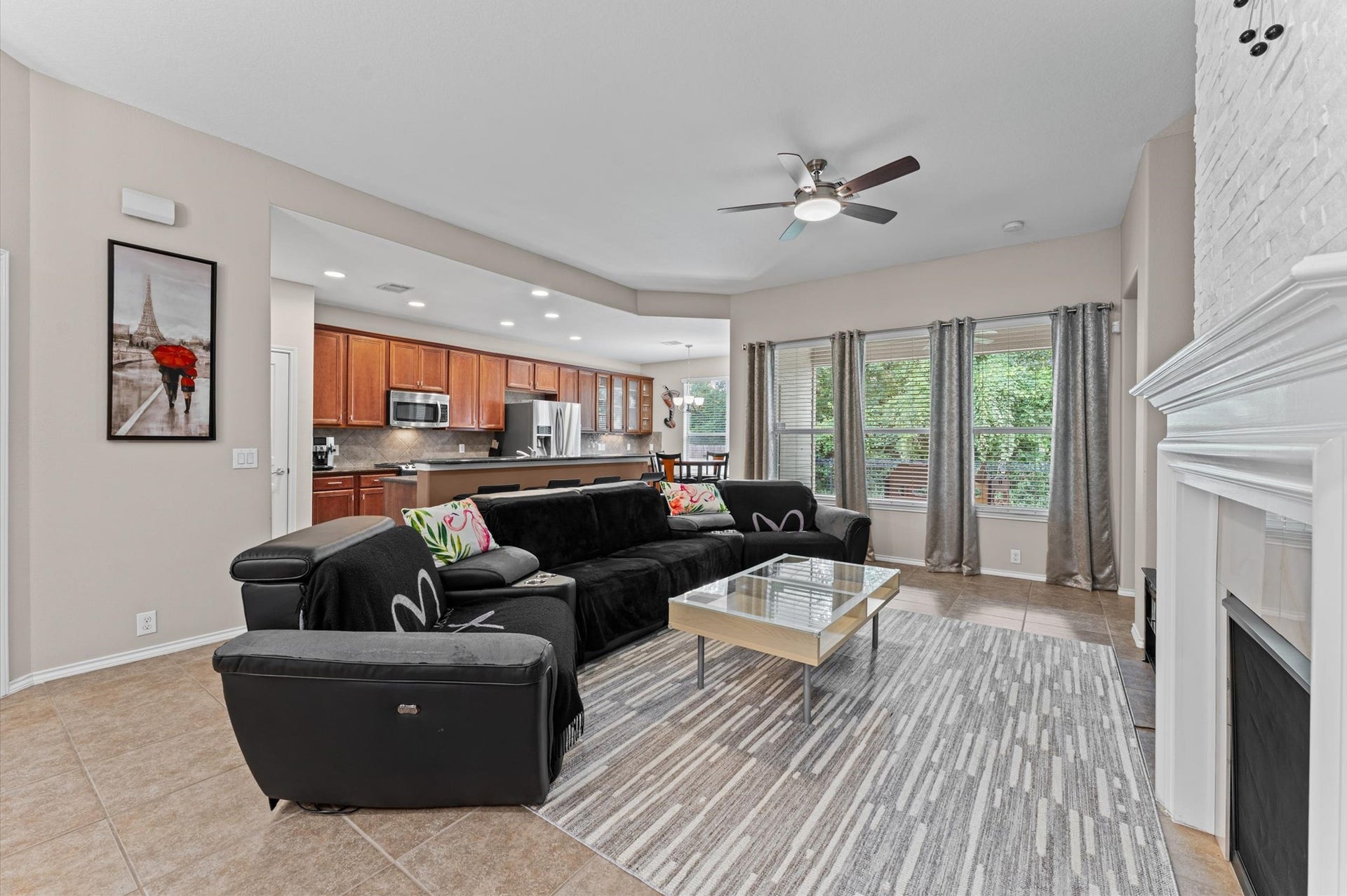 13423 Hartland Lake Lane, Houston, TX 77044 Spacious living area with a modern open floor plan, featuring a cozy fireplace, sleek tile flooring, and abundant natural light from large windows. The kitchen boasts stainless steel appliances and wooden cabinetry.