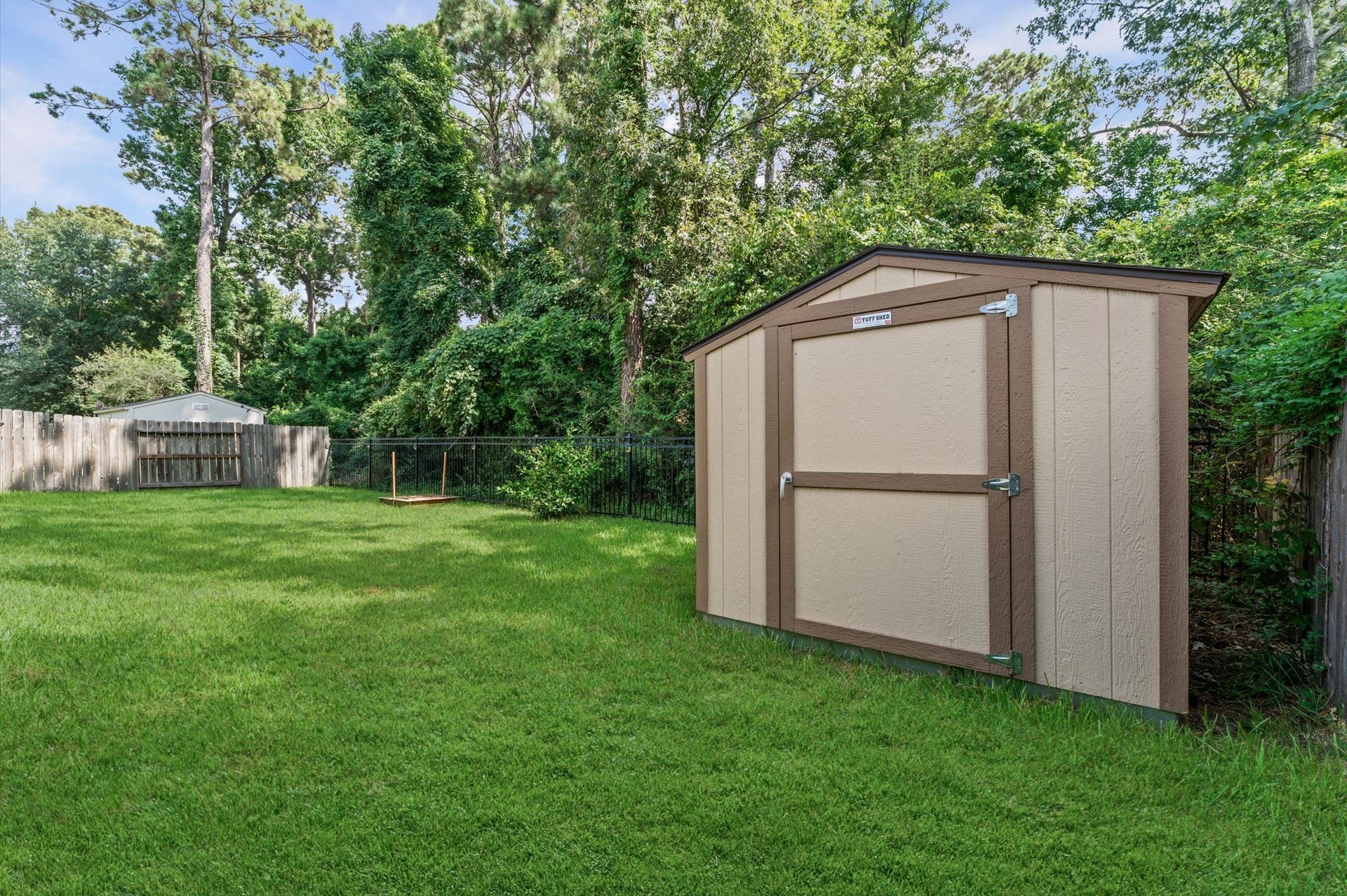 13423 Hartland Lake Lane, Houston, TX 77044 Spacious backyard with lush greenery, featuring a sturdy storage shed, perfect for organizing outdoor tools and equipment.