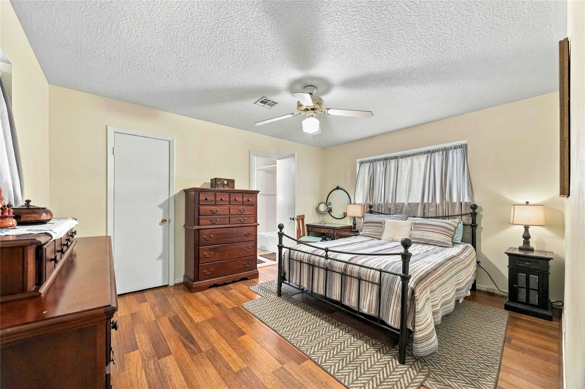 Enter the primary bedroom, where warm hardwood flooring and a large window create a bright, inviting space.
