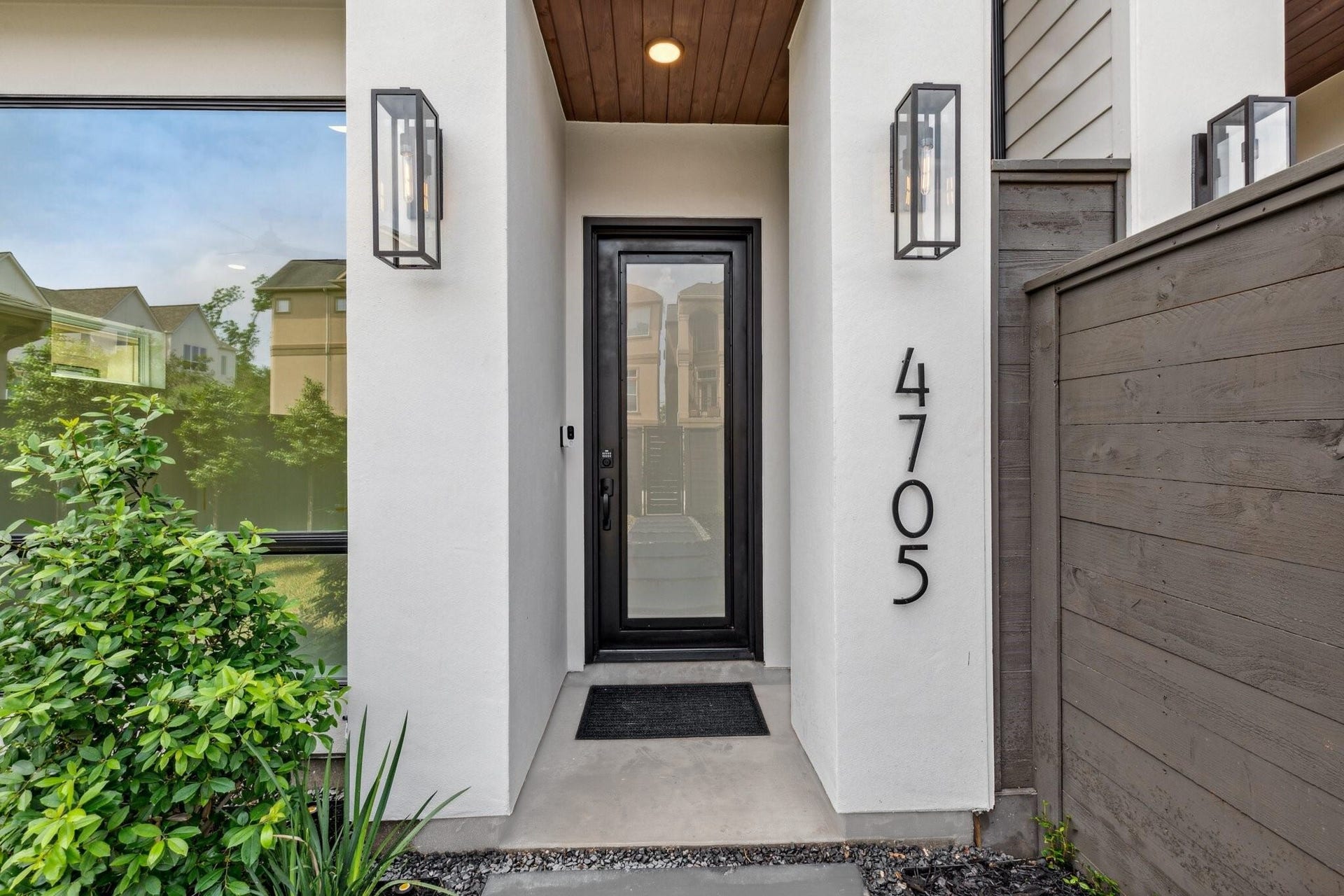 Welcome entrance through a striking custom steel front door, flanked by designer Visual Comfort exterior lights and a smart security doorbell for added peace of mind and style. Notice the wood paneled ceiling treatment.