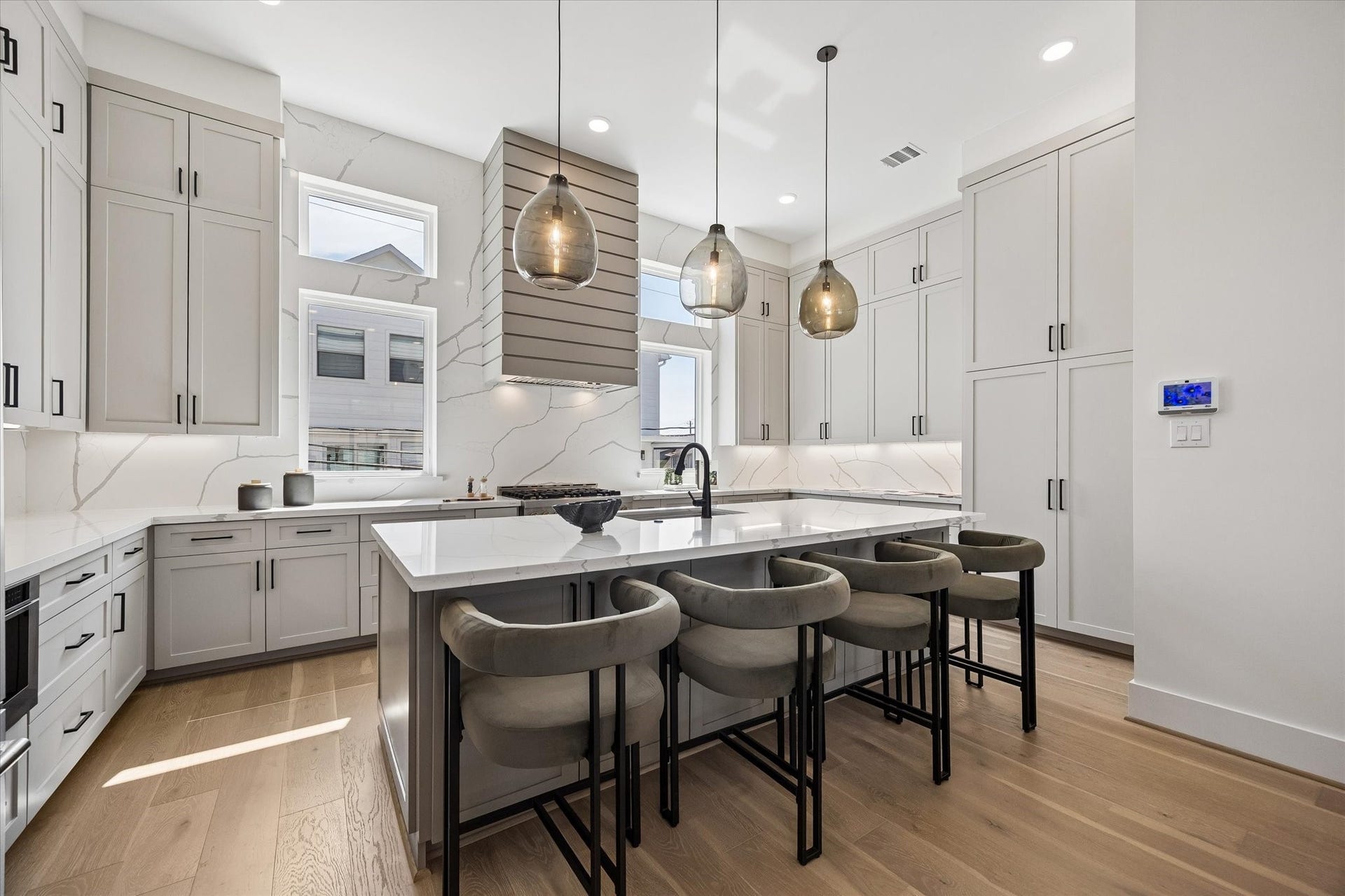 Another view of this stunning kitchen equipped w/ ample storage w/ custom-cabinetry built to the ceiling and large double door pantry.  Custom touches w/ pull-out spice racks and cookie tray divider. Natural light floods in through two large windows, beautifully complemented by Visual Comfort pendants and recessed lighting.