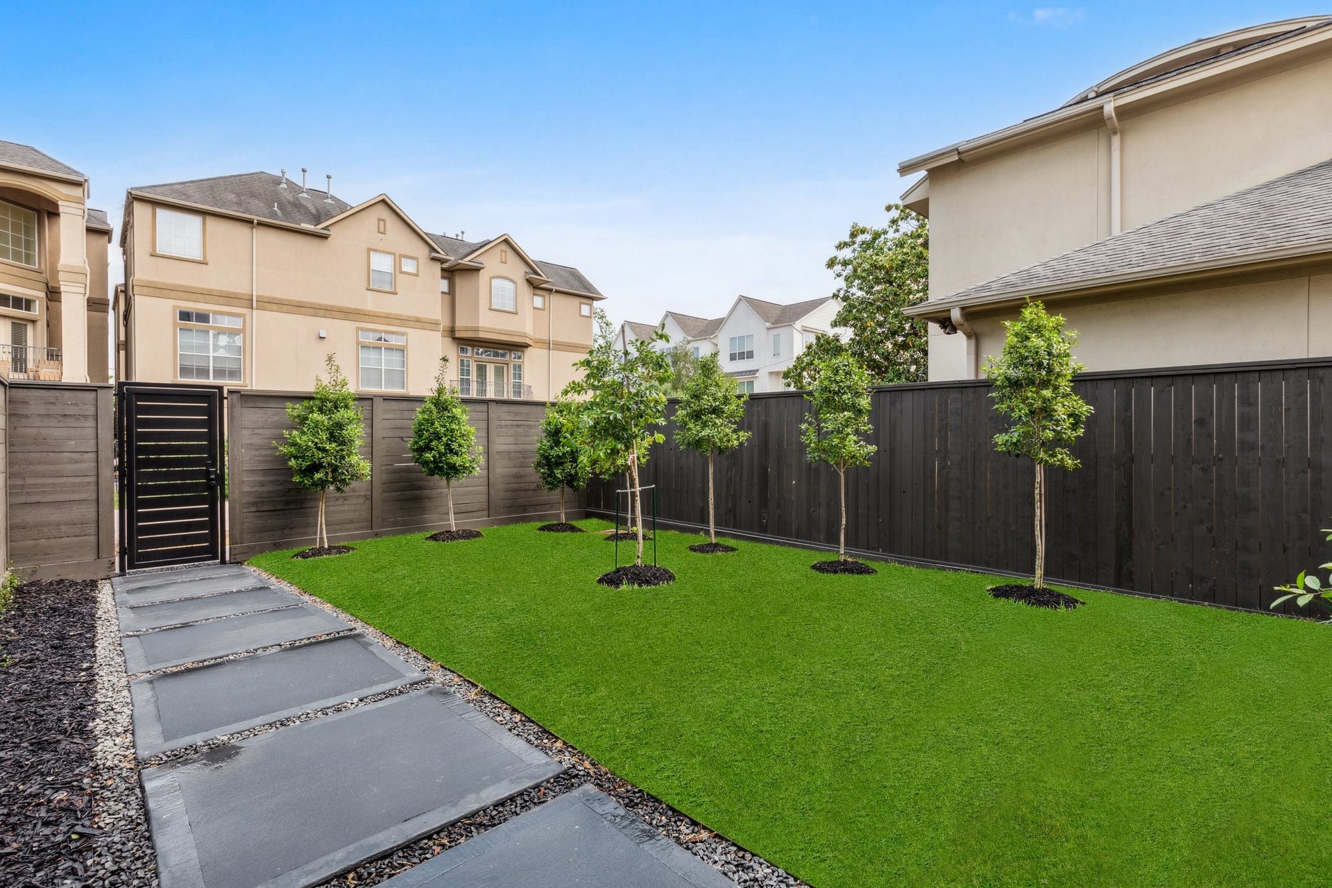 Another view of the spacious yard, framed by a cedar wood fence and a custom iron front door. A colored concrete walkway adds curb appeal as it leads you to the elegant entry.  Note: grass has been edited.