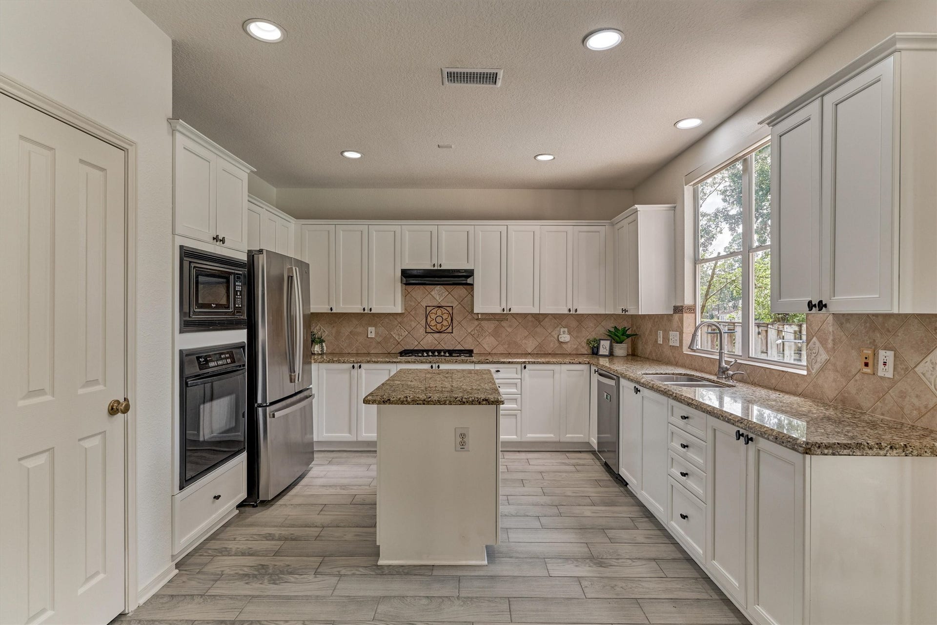 11 Vinca Trail, The Woodlands, TX 77382 The kitchen has lots of bright white cabinetry, a gas cooktop, large window over the sink and granite counters.