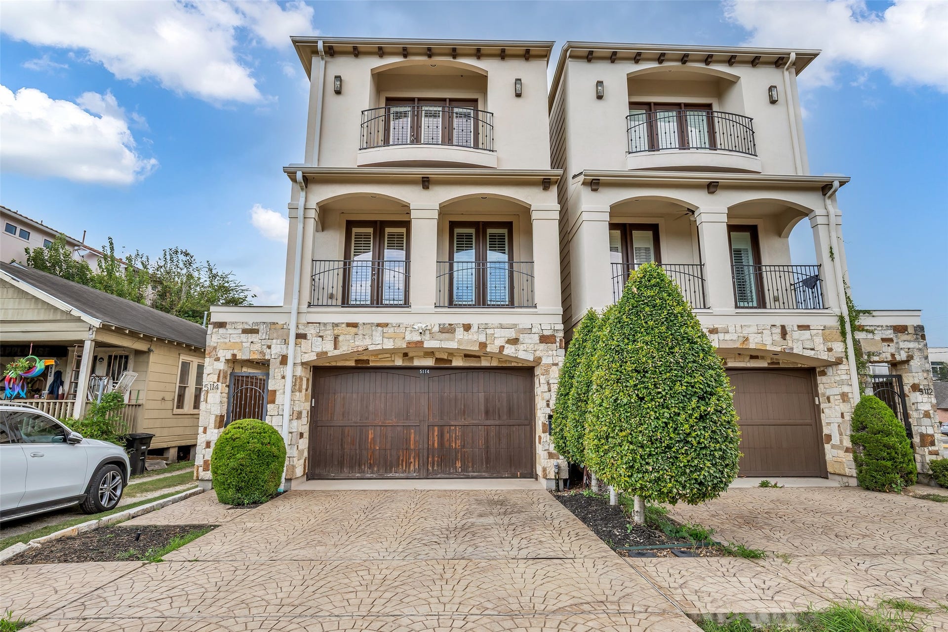 5114 Rose Street, Houston, TX 77007 Elegant multi-story home featuring a stone facade and two charming balconies, each above a spacious wooden garage door. Meticulous landscaping adds to the curb appeal.