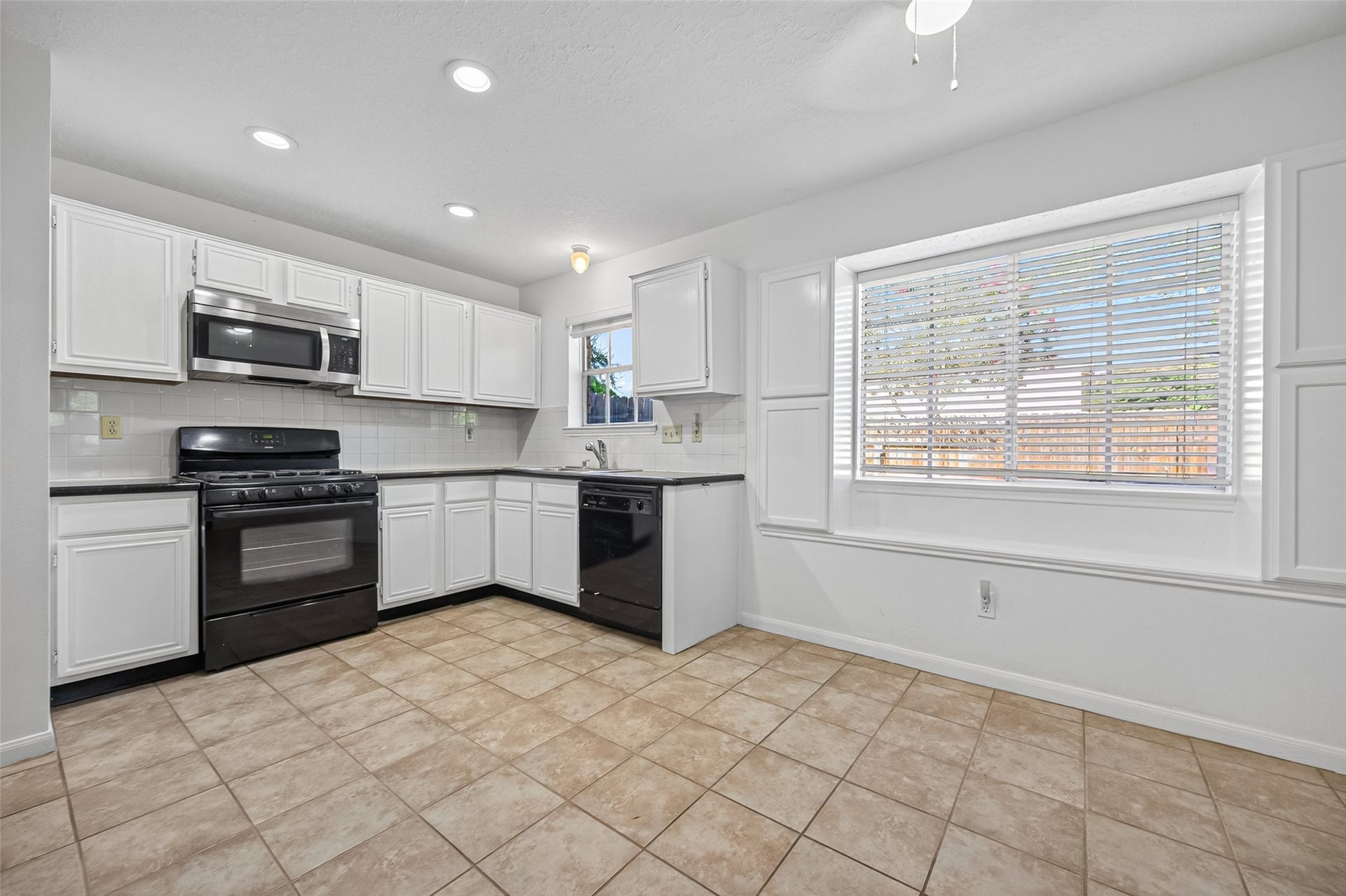 2703 Blue Mist Drive, Sugar Land, TX 77498 Spacious kitchen with sleek black countertops, modern stainless steel appliances, and ample white cabinetry, complemented by recessed lighting and tile flooring.