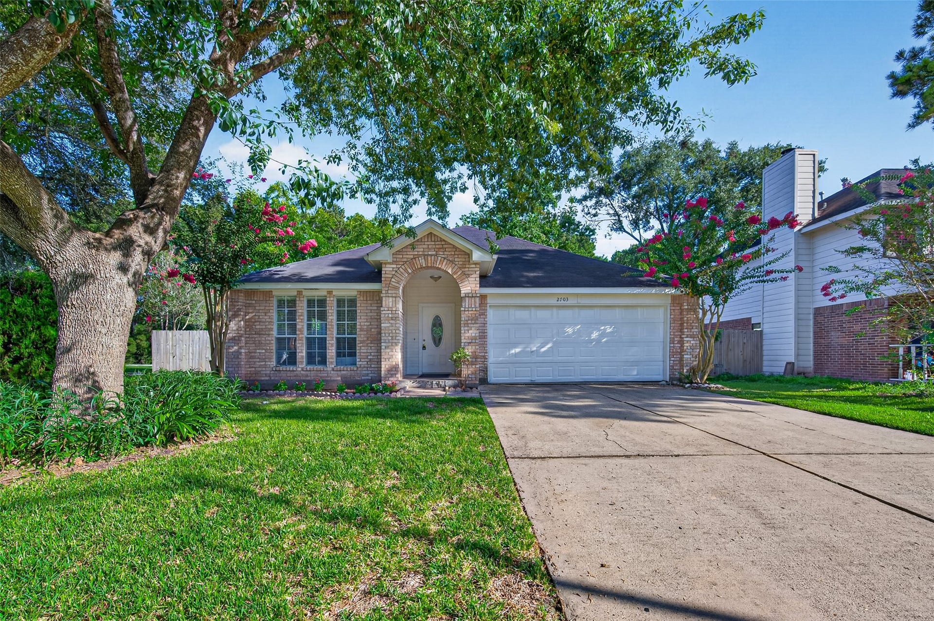 2703 Blue Mist Drive, Sugar Land, TX 77498 Charming brick home with a welcoming front yard, mature trees, and a spacious driveway leading to a two-car garage.