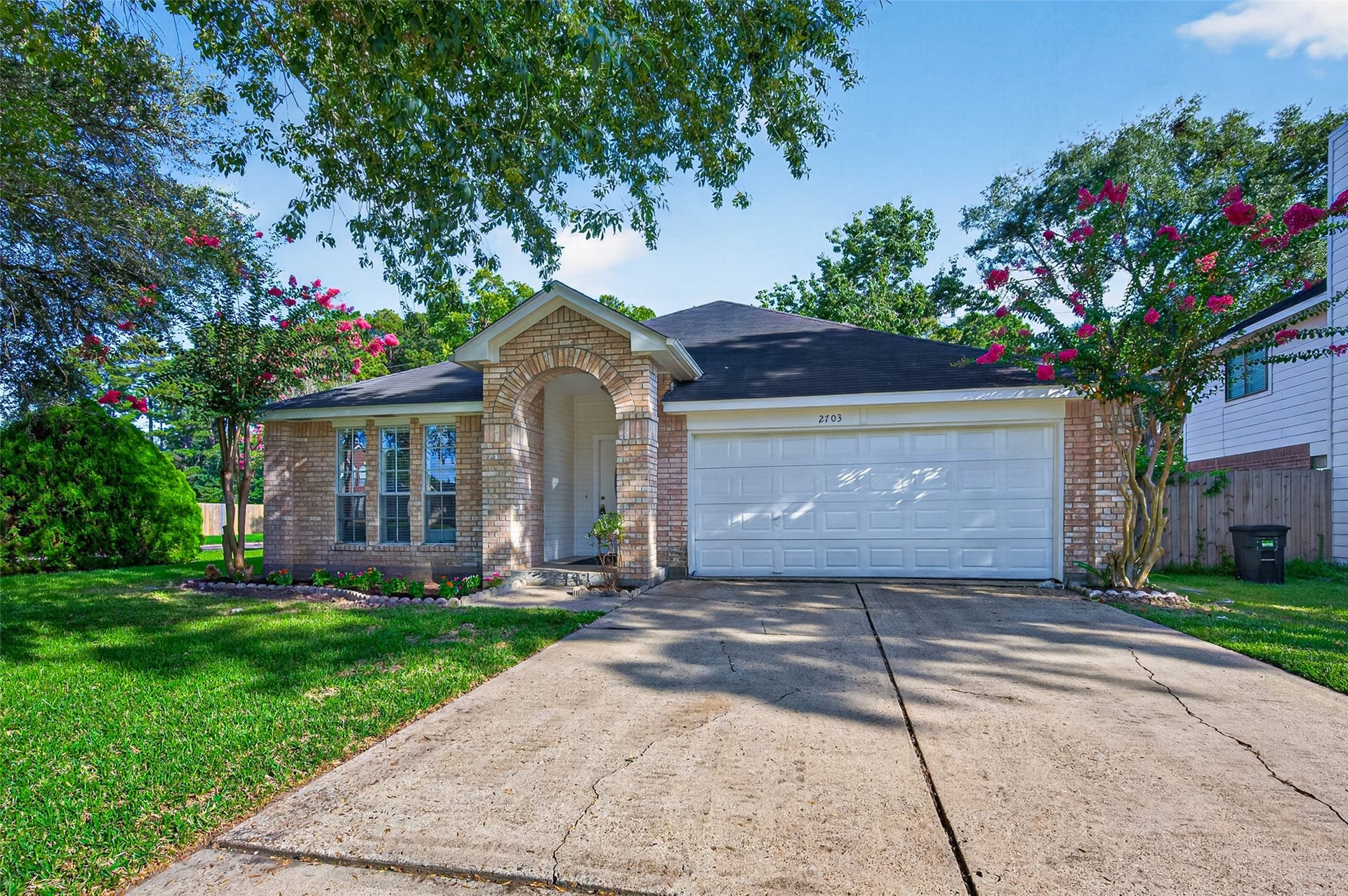 2703 Blue Mist Drive, Sugar Land, TX 77498 Charming brick home with a welcoming arched entryway, two-car garage, and lush landscaping accented by vibrant crepe myrtles.