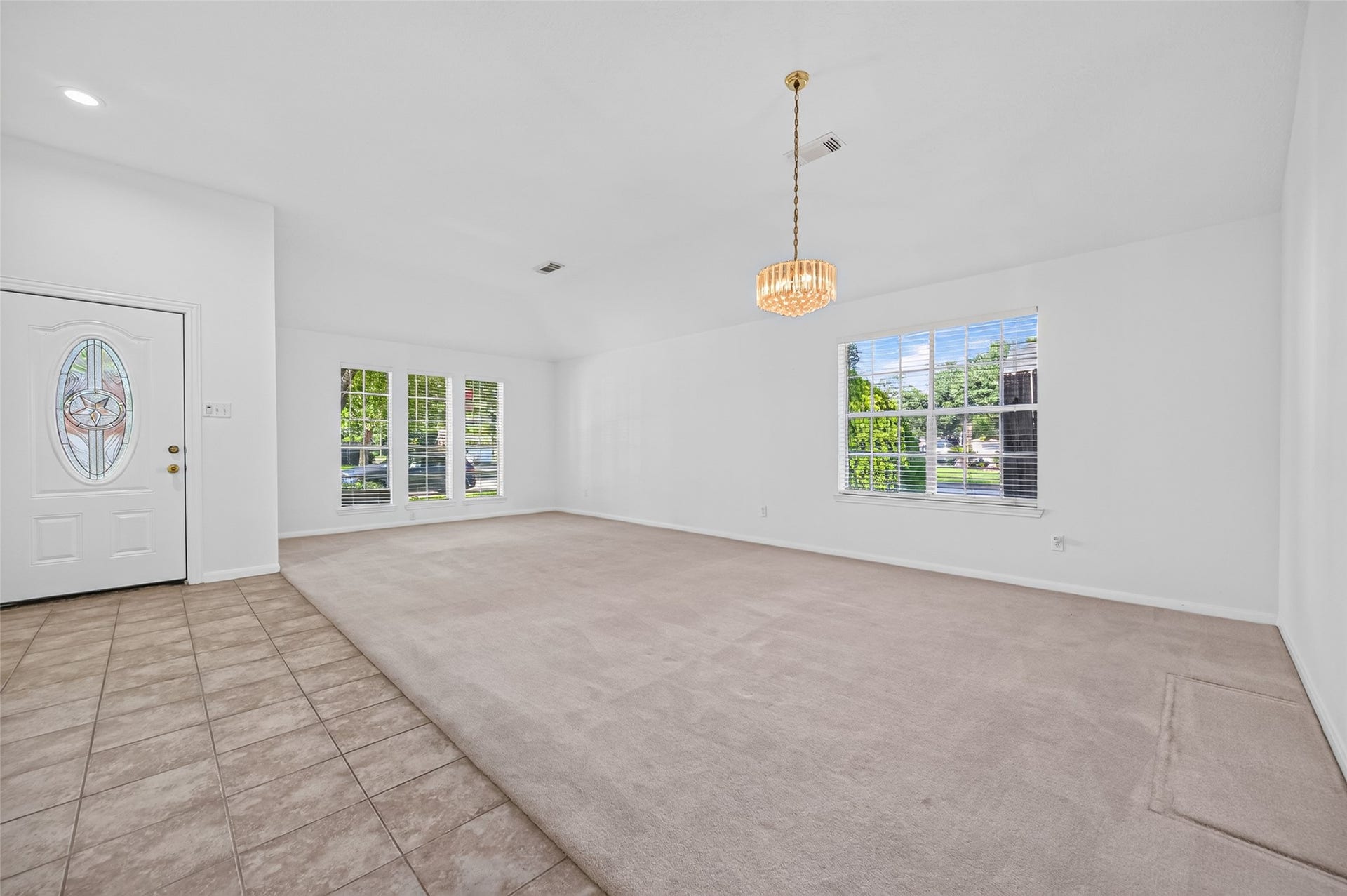 2703 Blue Mist Drive, Sugar Land, TX 77498 Spacious living area with a blend of carpet and tile flooring, featuring a large window for natural light and a stylish chandelier, leading to a bright hallway.