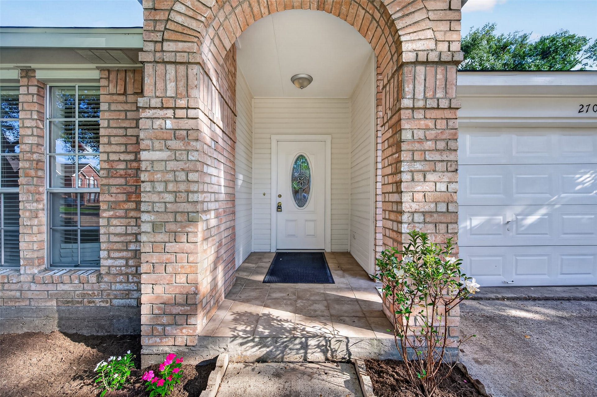 2703 Blue Mist Drive, Sugar Land, TX 77498 Charming brick home with a welcoming arched entryway, large windows, and a spacious two-car garage. Surrounded by lush greenery and vibrant flowering trees, it offers great curb appeal.