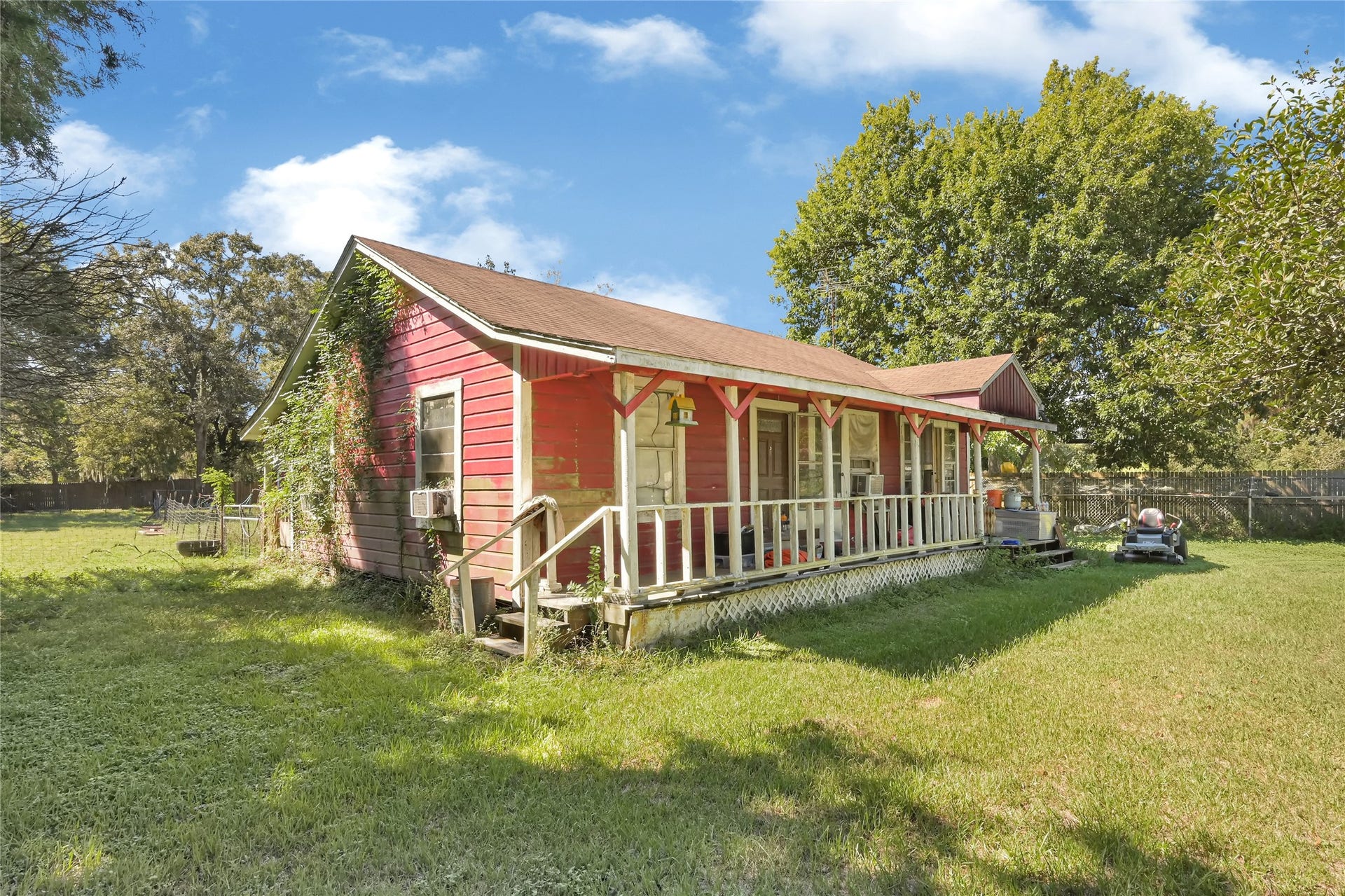 121 Patterson Road, Brazoria, TX 77422 Charming red cottage with a welcoming front porch, nestled in a spacious yard surrounded by mature trees.
