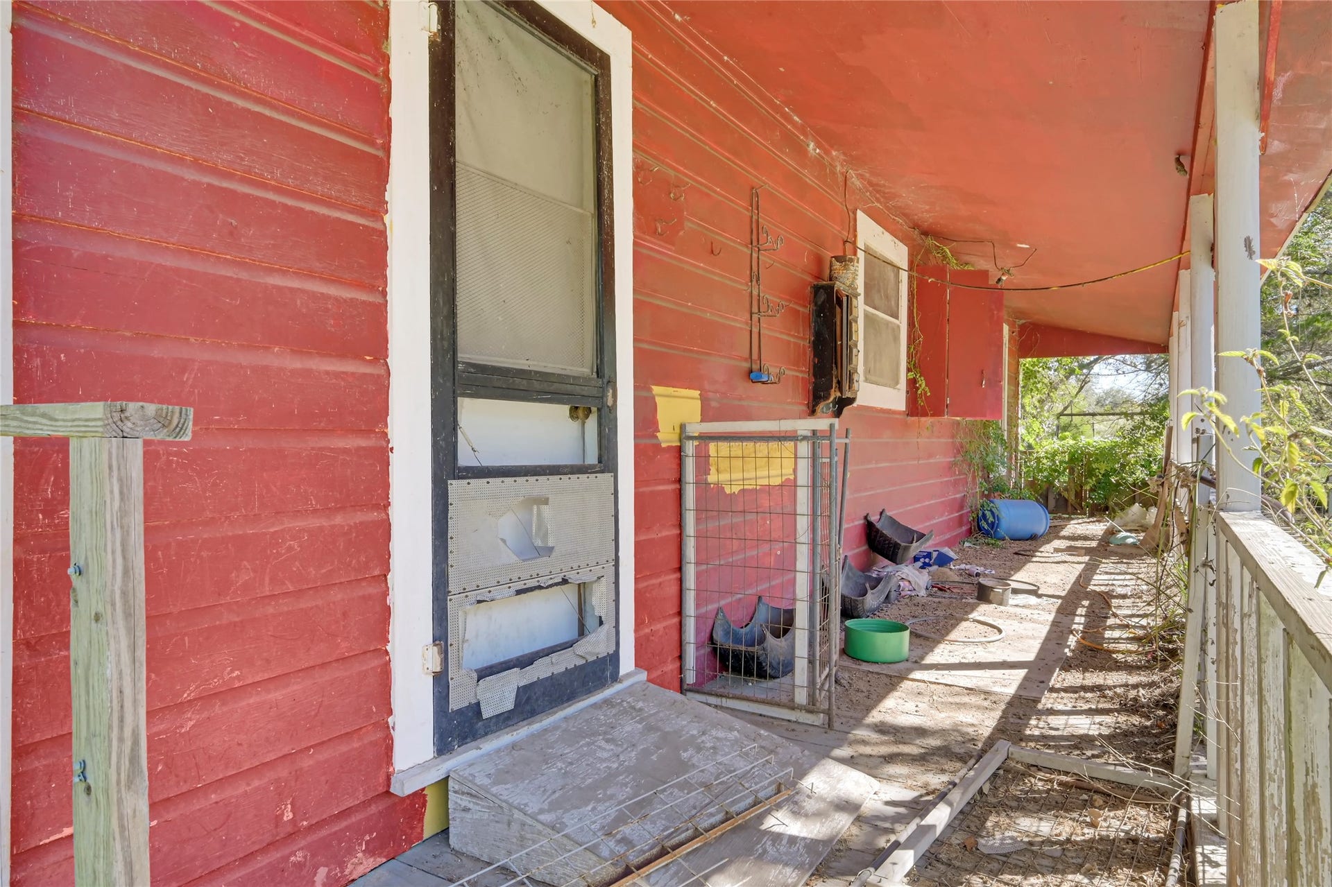 121 Patterson Road, Brazoria, TX 77422 Charming rustic porch with vibrant red siding, offering a cozy outdoor space surrounded by lush greenery, perfect for relaxation or creative renovation.