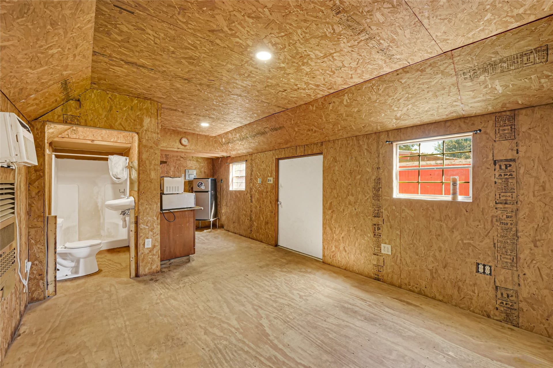 121 Patterson Road, Brazoria, TX 77422 Spacious room with plywood walls featuring a small kitchenette and a convenient half-bath, offering a blank slate for customization.