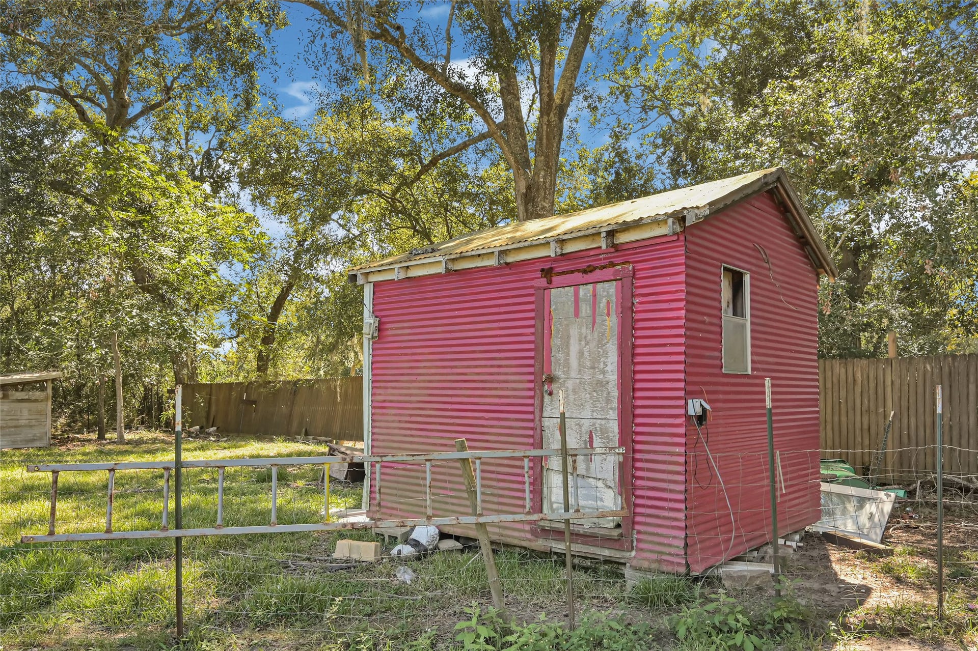 121 Patterson Road, Brazoria, TX 77422 Charming rustic shed with vibrant pink siding set amidst a lush, fenced backyard, offering potential for creative outdoor projects.