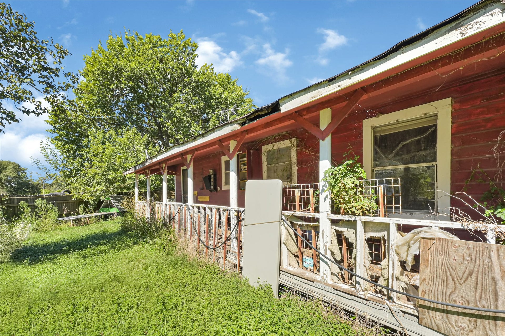 121 Patterson Road, Brazoria, TX 77422 Charming rustic home with a classic red exterior and spacious wrap-around porch, set amidst lush greenery. Perfect for those seeking a renovation project with character.