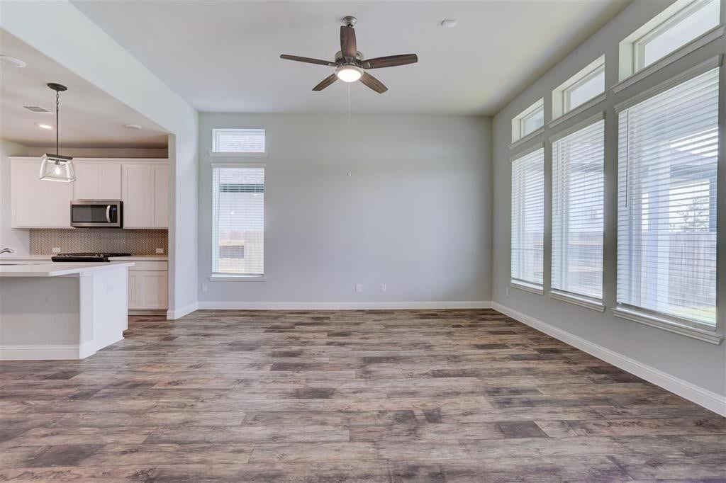 23715 Ruby Bramble Trail, Katy, TX 77493 Spacious open-concept living area with abundant natural light, featuring large windows, elegant wood-look flooring, and a modern ceiling fan. The adjacent kitchen boasts sleek cabinetry and contemporary appliances.