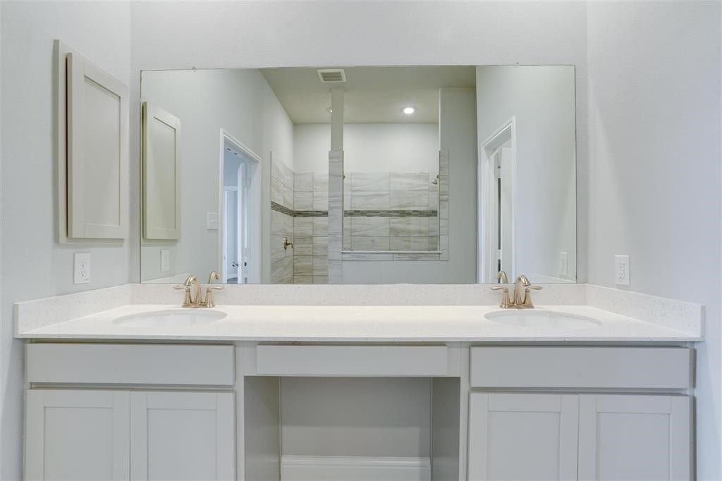 23715 Ruby Bramble Trail, Katy, TX 77493 Elegant primary bathroom featuring a spacious double vanity with sleek countertops and modern fixtures, complemented by a large mirror and a stylish walk-in shower in the background.