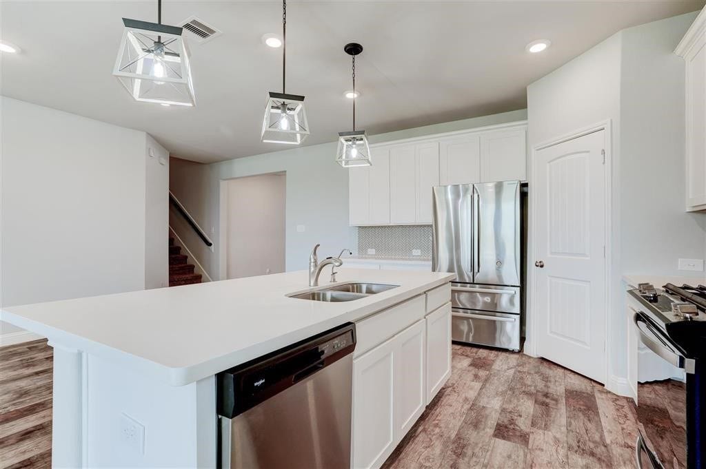 23715 Ruby Bramble Trail, Katy, TX 77493 Modern kitchen with sleek stainless steel appliances, a large island with a sink, and elegant pendant lighting, complemented by wood-look flooring.