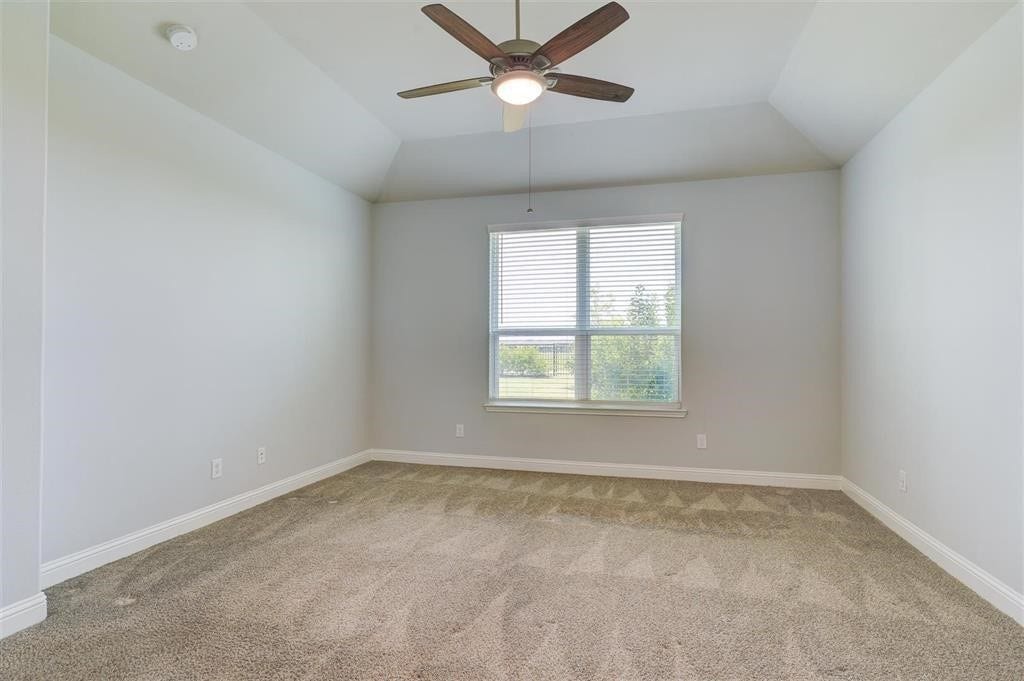 23715 Ruby Bramble Trail, Katy, TX 77493 Spacious primary bedroom with plush carpet, light gray walls, a large window offering natural light, and a ceiling fan for added comfort. Located on the first floor.