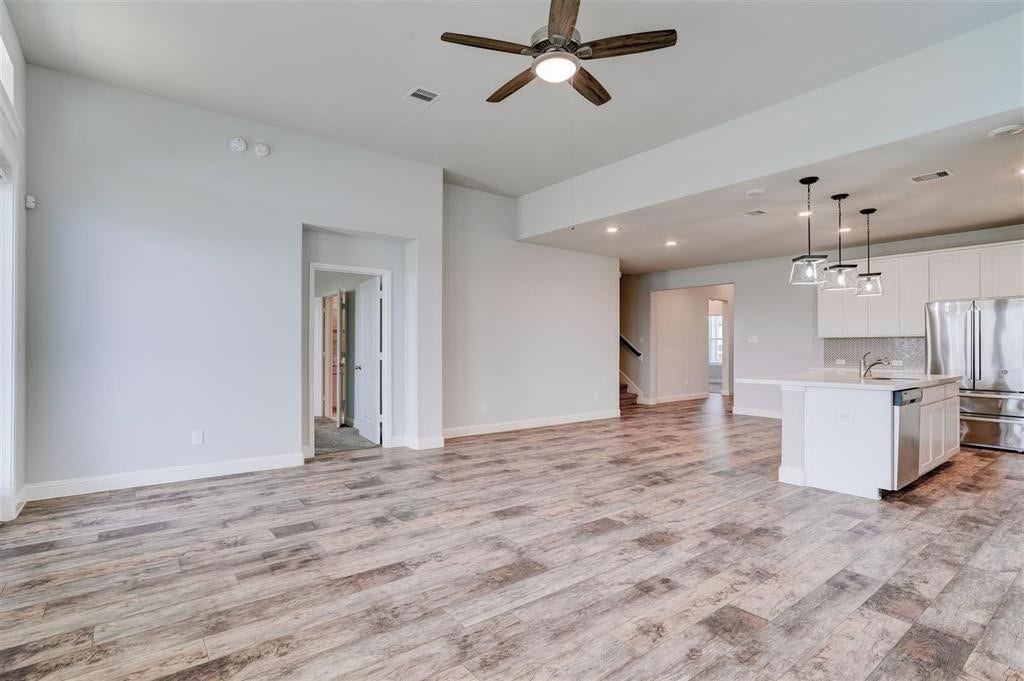 23715 Ruby Bramble Trail, Katy, TX 77493 Open-concept living area featuring elegant wood-look flooring, a modern kitchen with stainless steel appliances, and stylish pendant lighting.