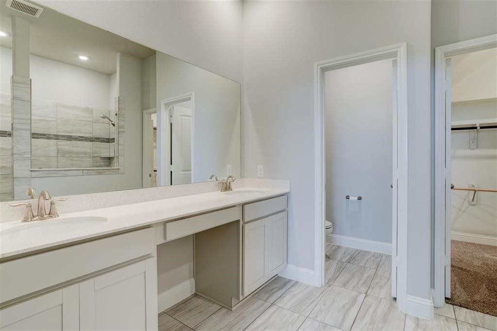 23715 Ruby Bramble Trail, Katy, TX 77493 Spacious primary bathroom featuring a long double vanity with sleek countertops, modern fixtures, and an adjacent walk-in closet for ample storage.