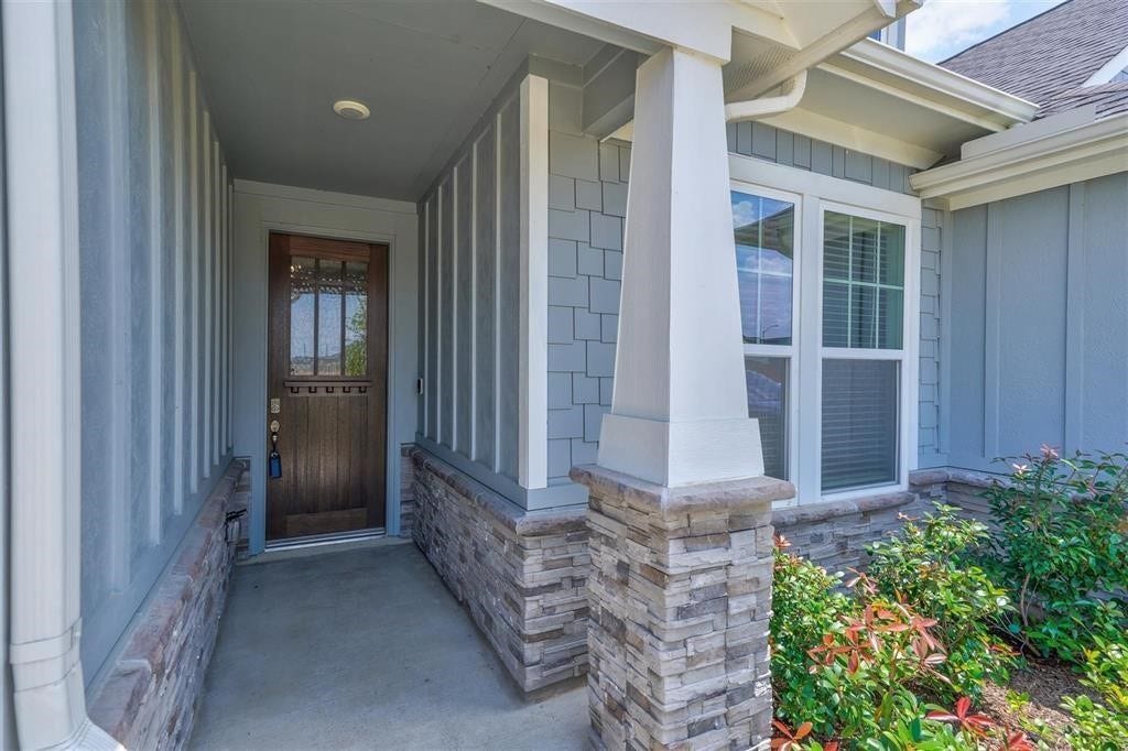 23715 Ruby Bramble Trail, Katy, TX 77493 Charming entryway with stone accents and a welcoming wooden door, complemented by lush greenery and elegant siding.