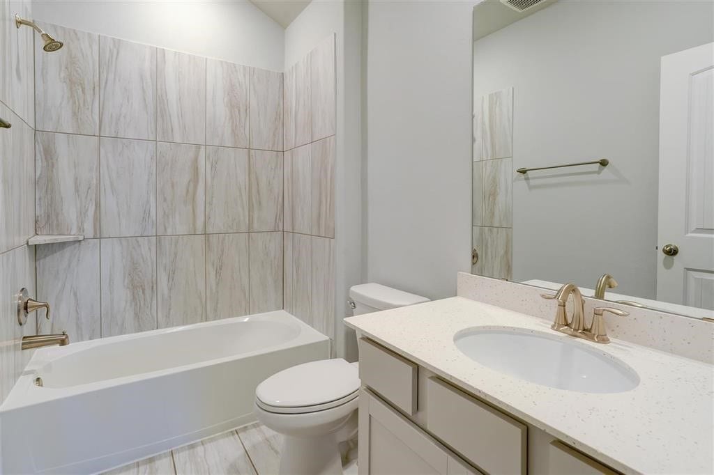 23715 Ruby Bramble Trail, Katy, TX 77493 Elegant secondary bathroom featuring a sleek vanity with quartz countertop, a spacious tub with modern tile surround, and stylish gold fixtures.