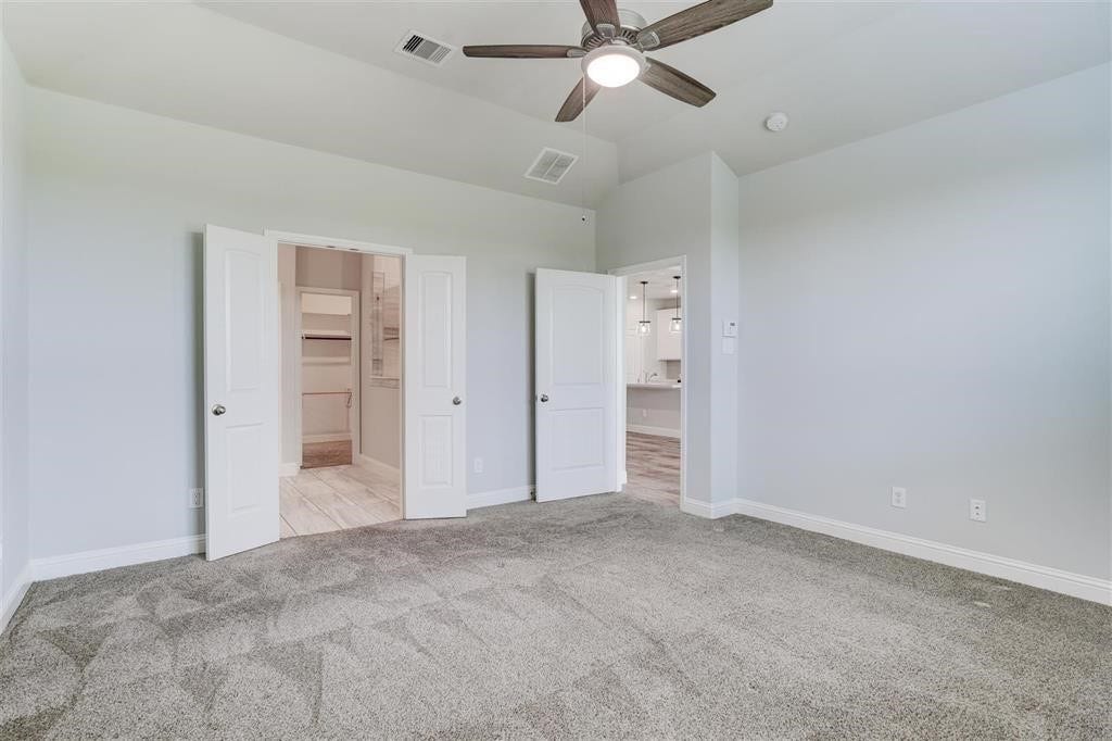 23715 Ruby Bramble Trail, Katy, TX 77493 Spacious primary bedroom with plush carpeting, a modern ceiling fan, and direct access to a walk-in closet and en-suite bathroom through elegant double doors.