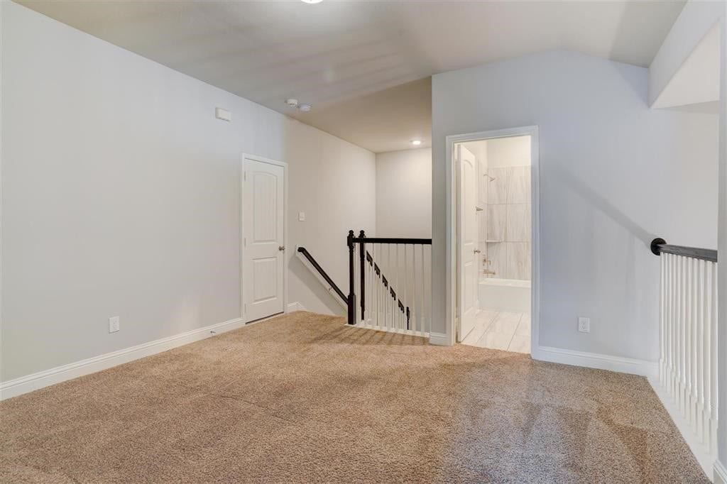 23715 Ruby Bramble Trail, Katy, TX 77493 Spacious carpeted game room with neutral tones, featuring access to a modern bathroom and an elegant railing overlooking the staircase.